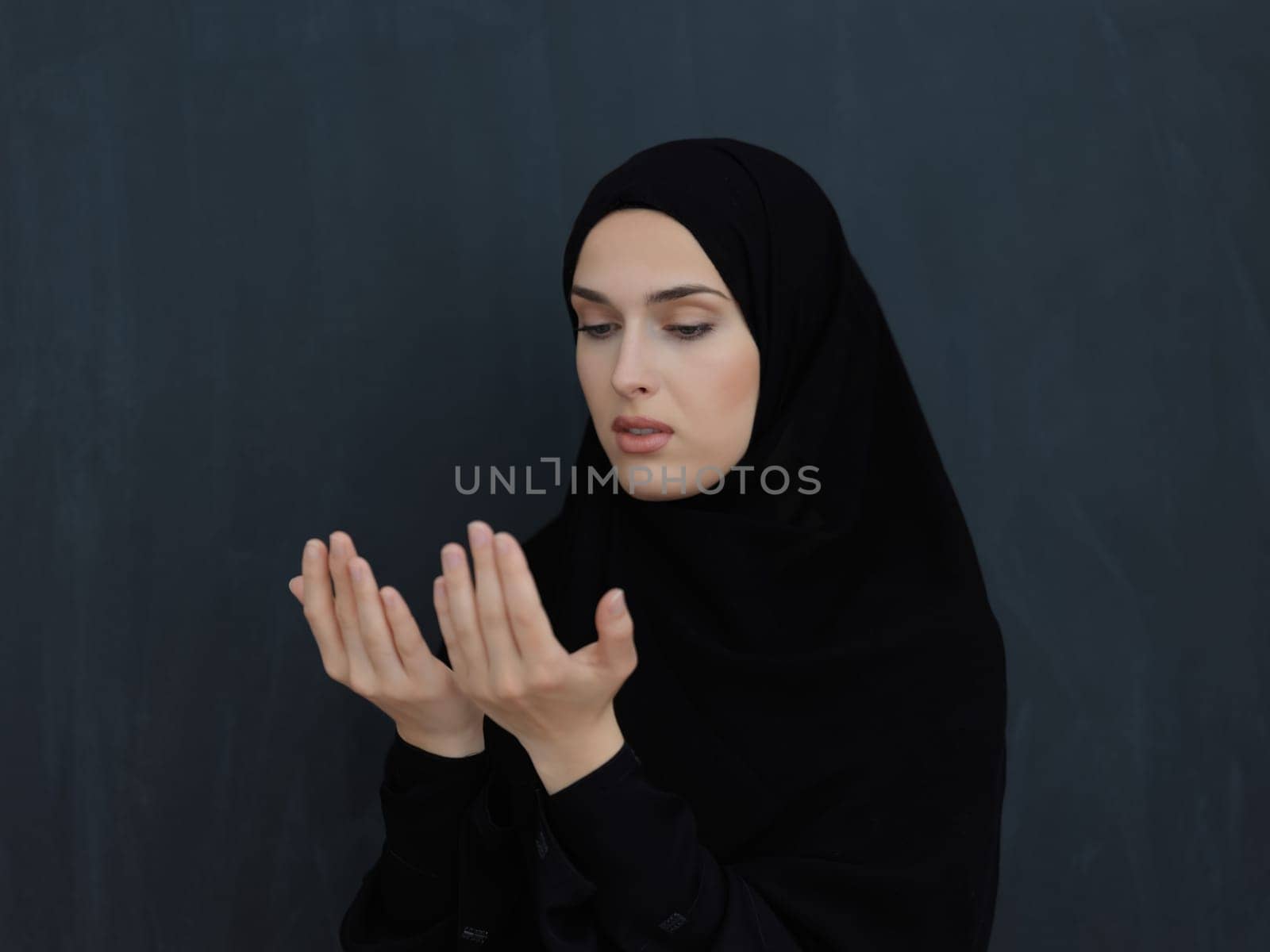 Portrait of young Muslim woman making dua. Arabian girl wearing abaya keeps hands in praying gesture. Representing worship to God and Ramadan Kareem concept