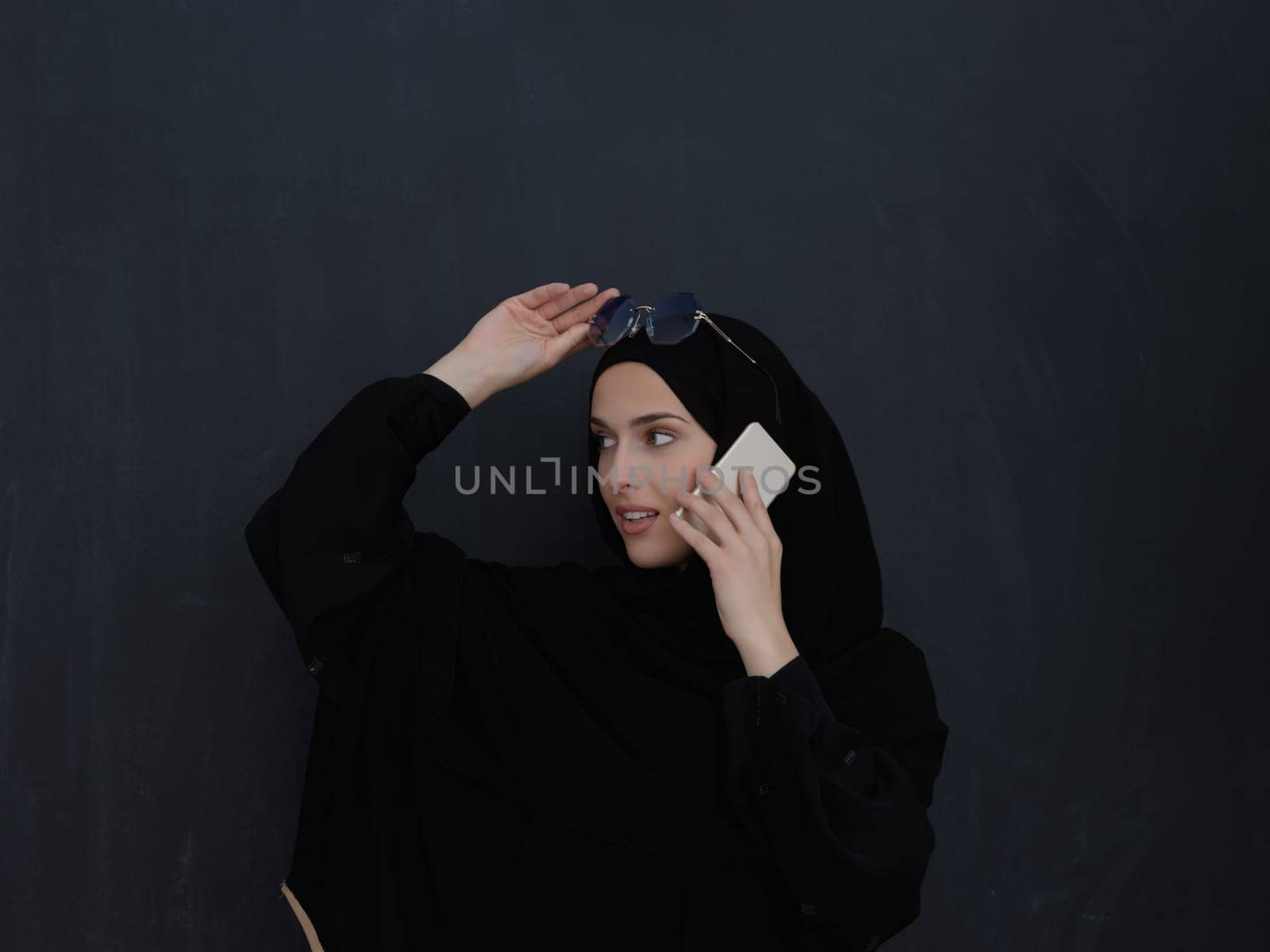 Young muslim businesswoman in traditional clothes or abaya talking on the smartphone. Arab woman in front of black chalkboard and representing techology, islamic fashion and Ramadan kareem concept