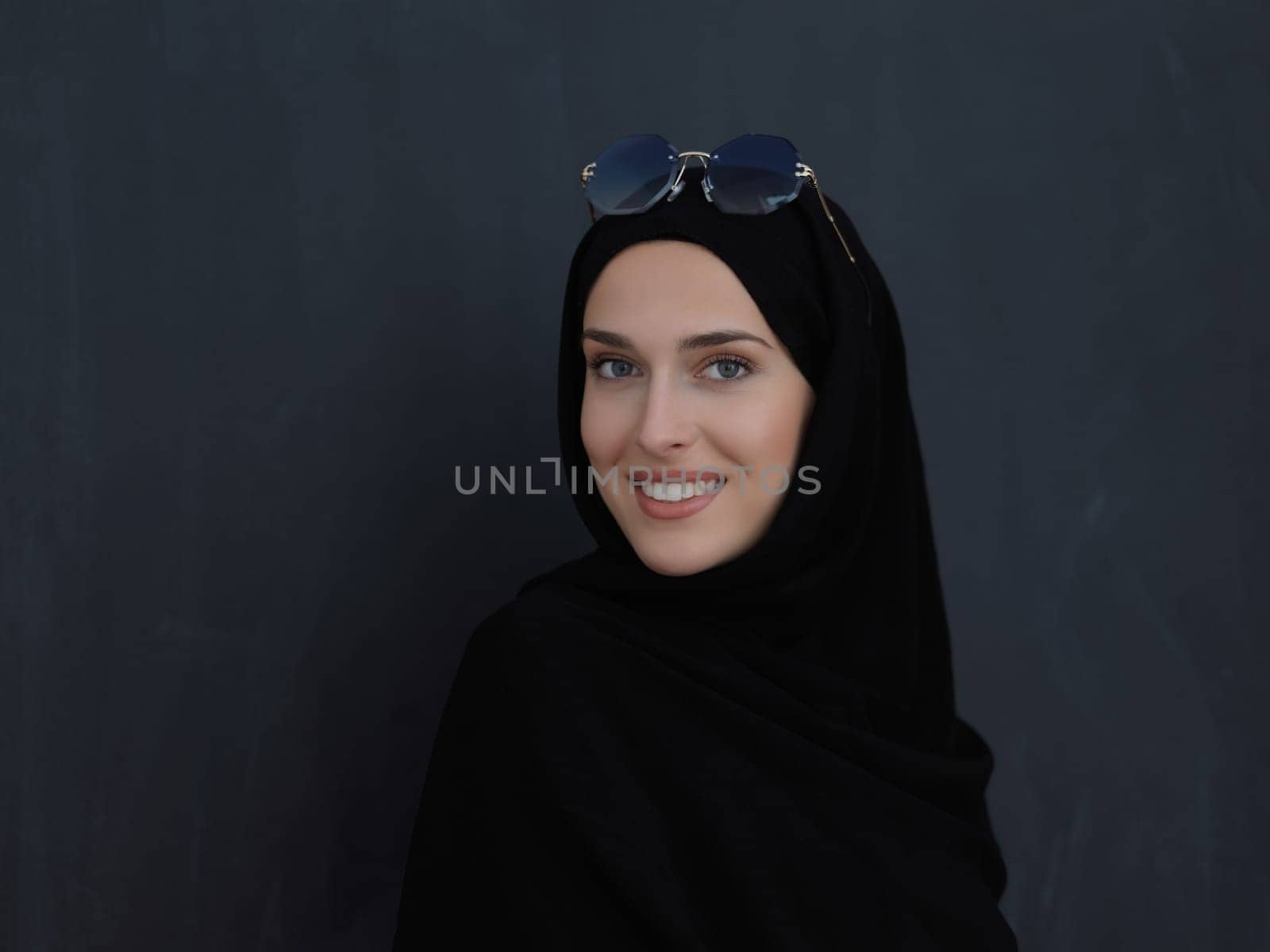 Young muslim in traditional clothes or abaya and sunglasses posing in front of black chalkboard. Arab woman representing modern arabic lifestyle, islamic fashion and Ramadan kareem concept