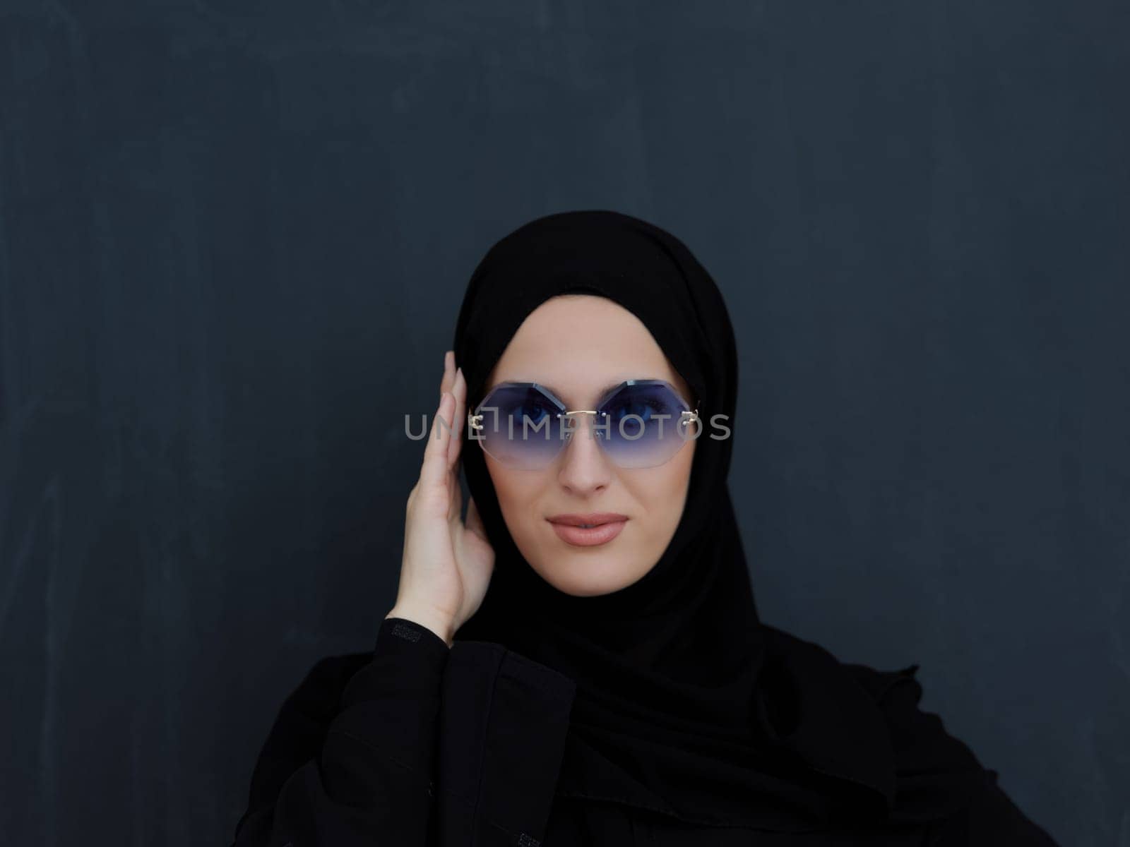 Young muslim in traditional clothes or abaya and sunglasses posing in front of black chalkboard. Arab woman representing modern arabic lifestyle, islamic fashion and Ramadan kareem concept