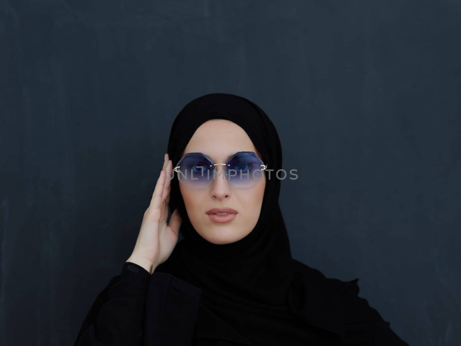 Young muslim in traditional clothes or abaya and sunglasses posing in front of black chalkboard. Arab woman representing modern arabic lifestyle, islamic fashion and Ramadan kareem concept