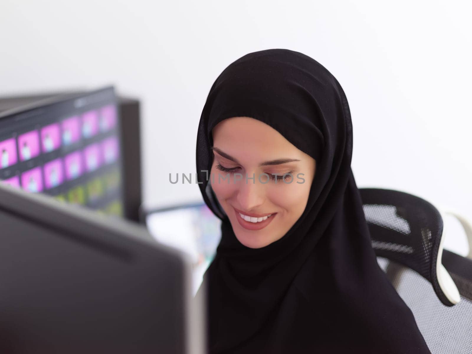 Portrait of young muslim female graphic designer. Hijab girl with the two monitors in background showing her work. Technology concept