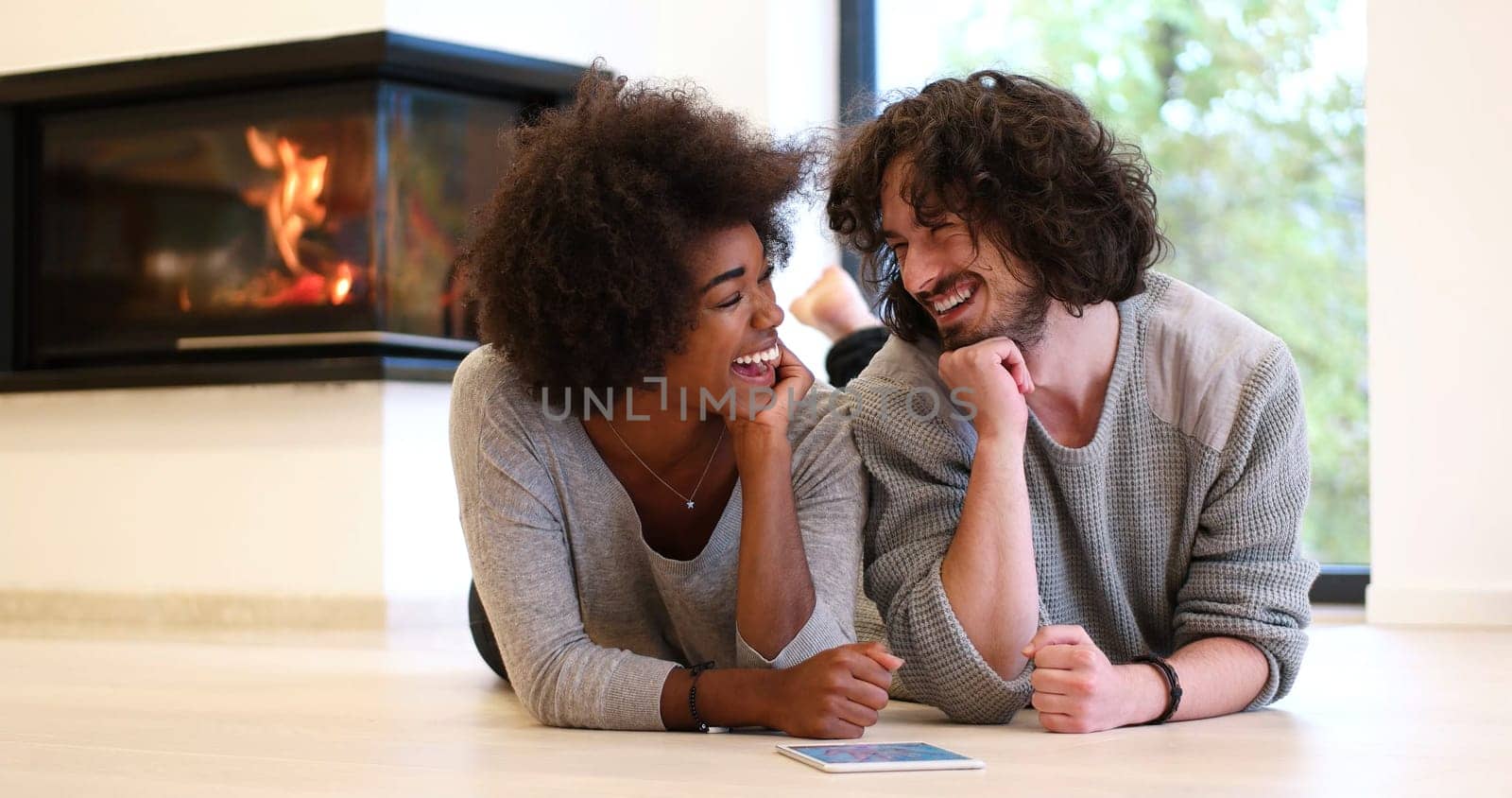 beautiful young multiethnic couple lying on the floor of their luxury home in front of fireplace at autumn day