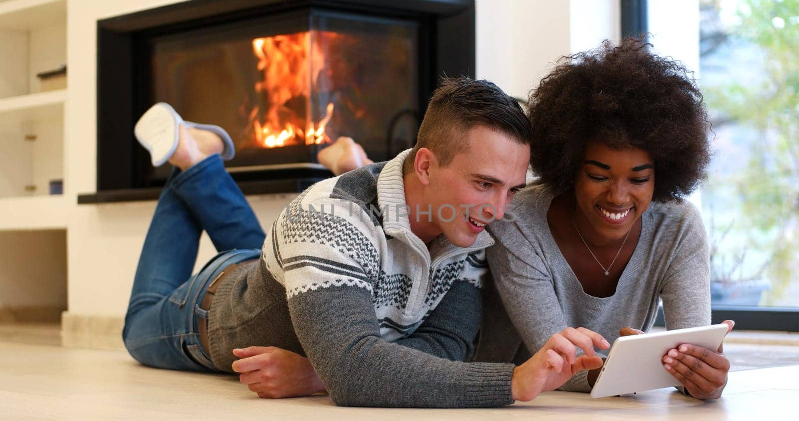 beautiful young multiethnic couple using tablet computer on the floor of their luxury home in front of fireplace at autumn day