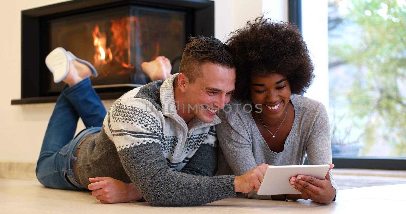 beautiful young multiethnic couple using tablet computer on the floor of their luxury home in front of fireplace at autumn day