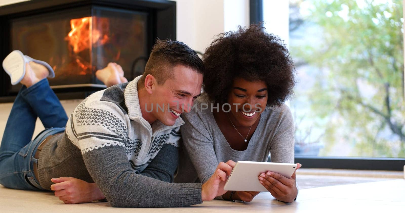 beautiful young multiethnic couple using tablet computer on the floor of their luxury home in front of fireplace at autumn day