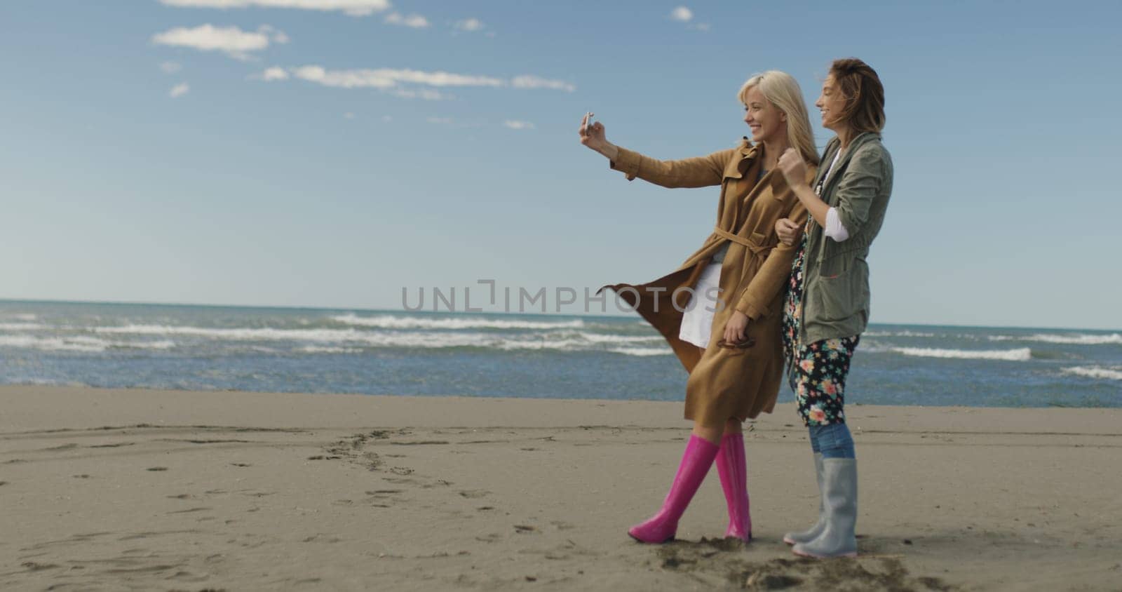 Friends making selfie. two beautiful young women making selfie at autumn day on the beach