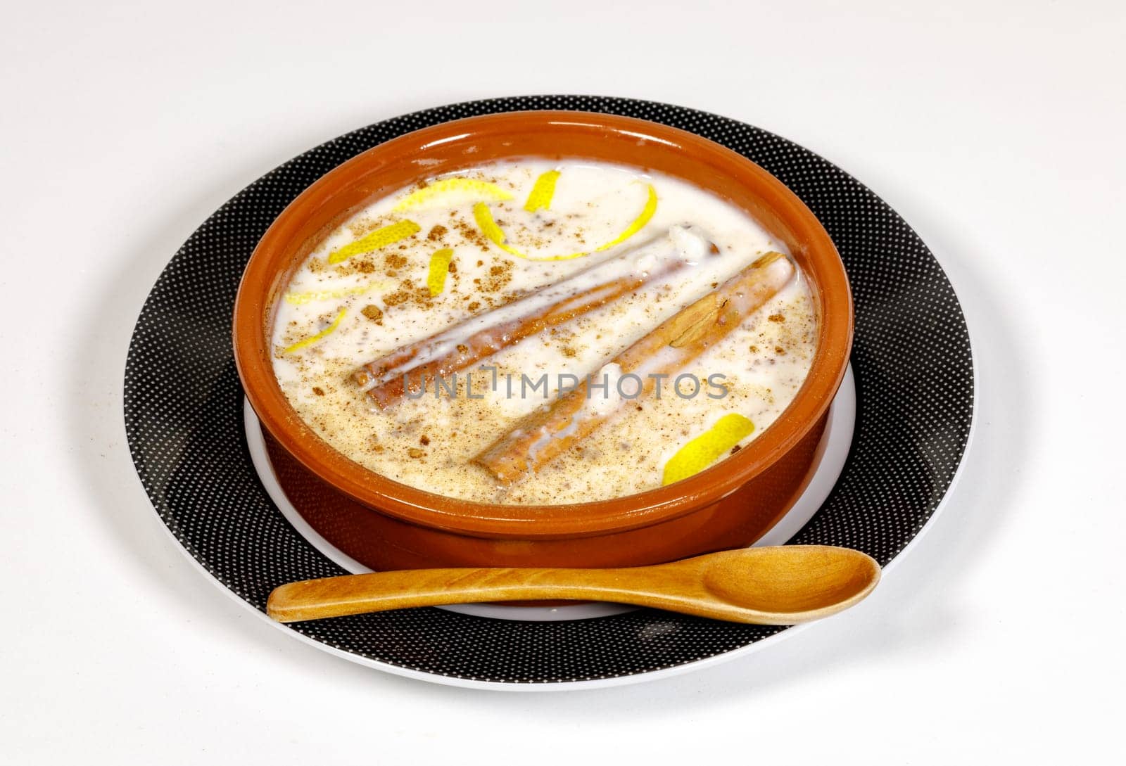 Dish of rice pudding with grated cinnamon, with lemon scratches. on plate and wooden spoon