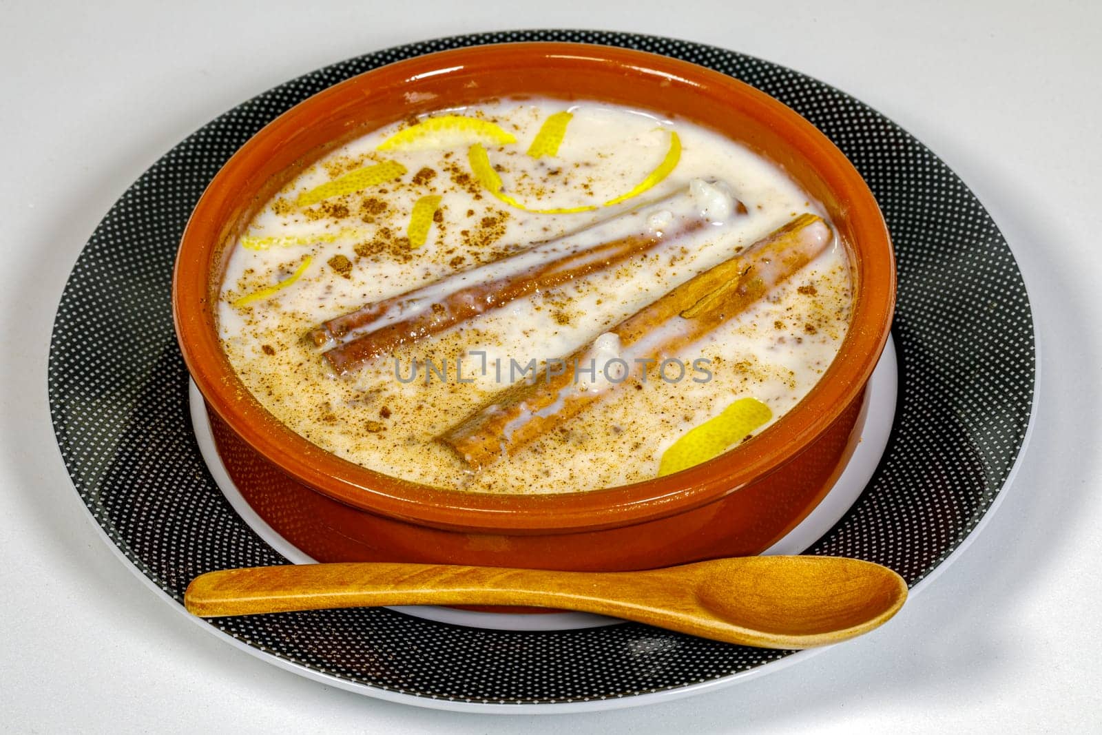 Dish of rice pudding with grated cinnamon, with lemon scratches. on plate and wooden spoon