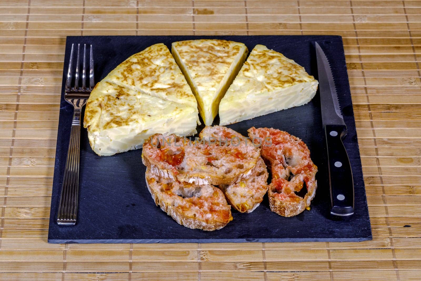 A triangle of potato Spanish omelette prepared on slate plate and covered with bread with tomato