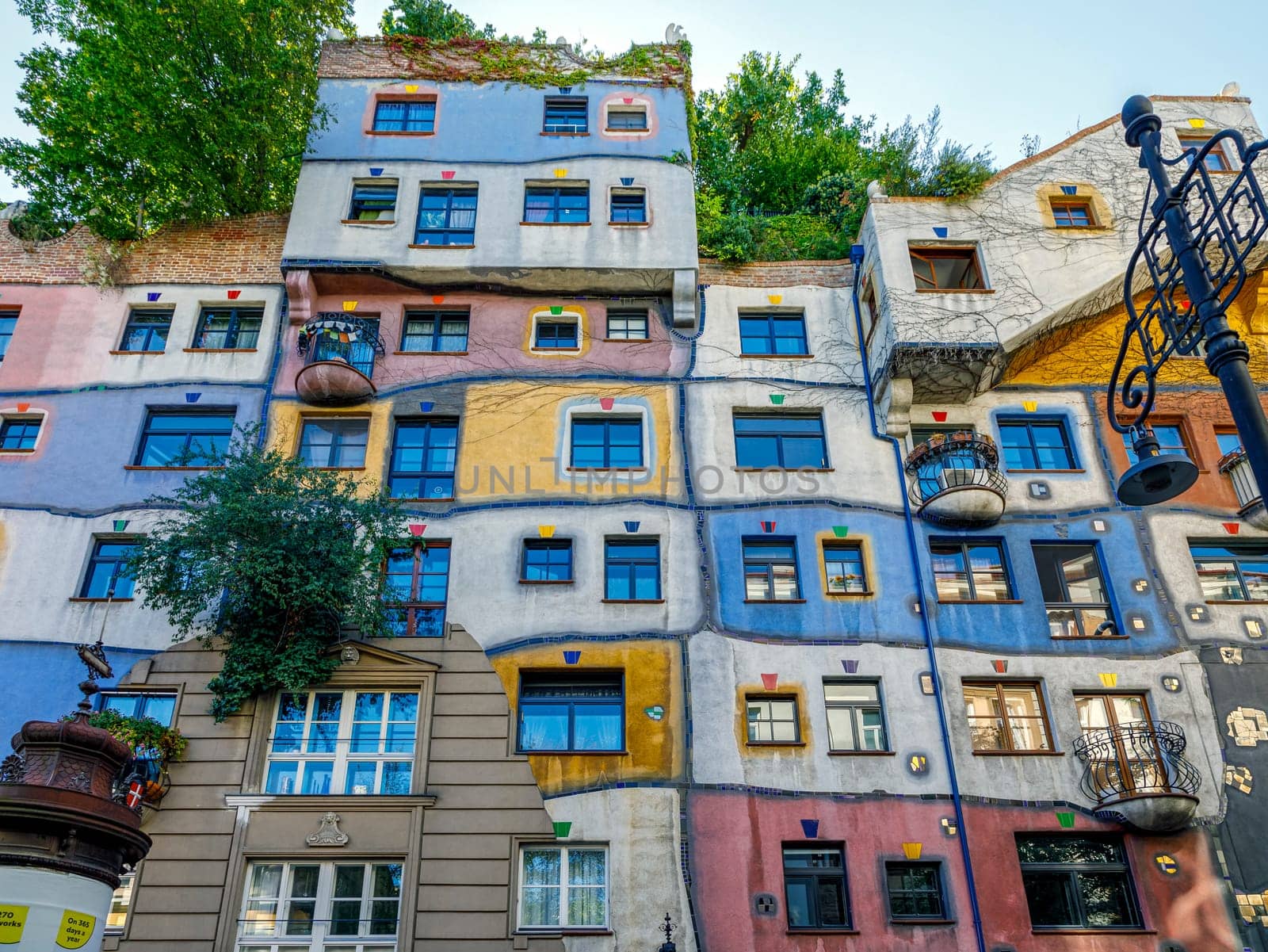 Vienna, Austria - September 16, 2019: Hundertwasserhaus apartment block has colorful facade, undulating floors, roof covered with earth and grass, large trees growing from inside the rooms