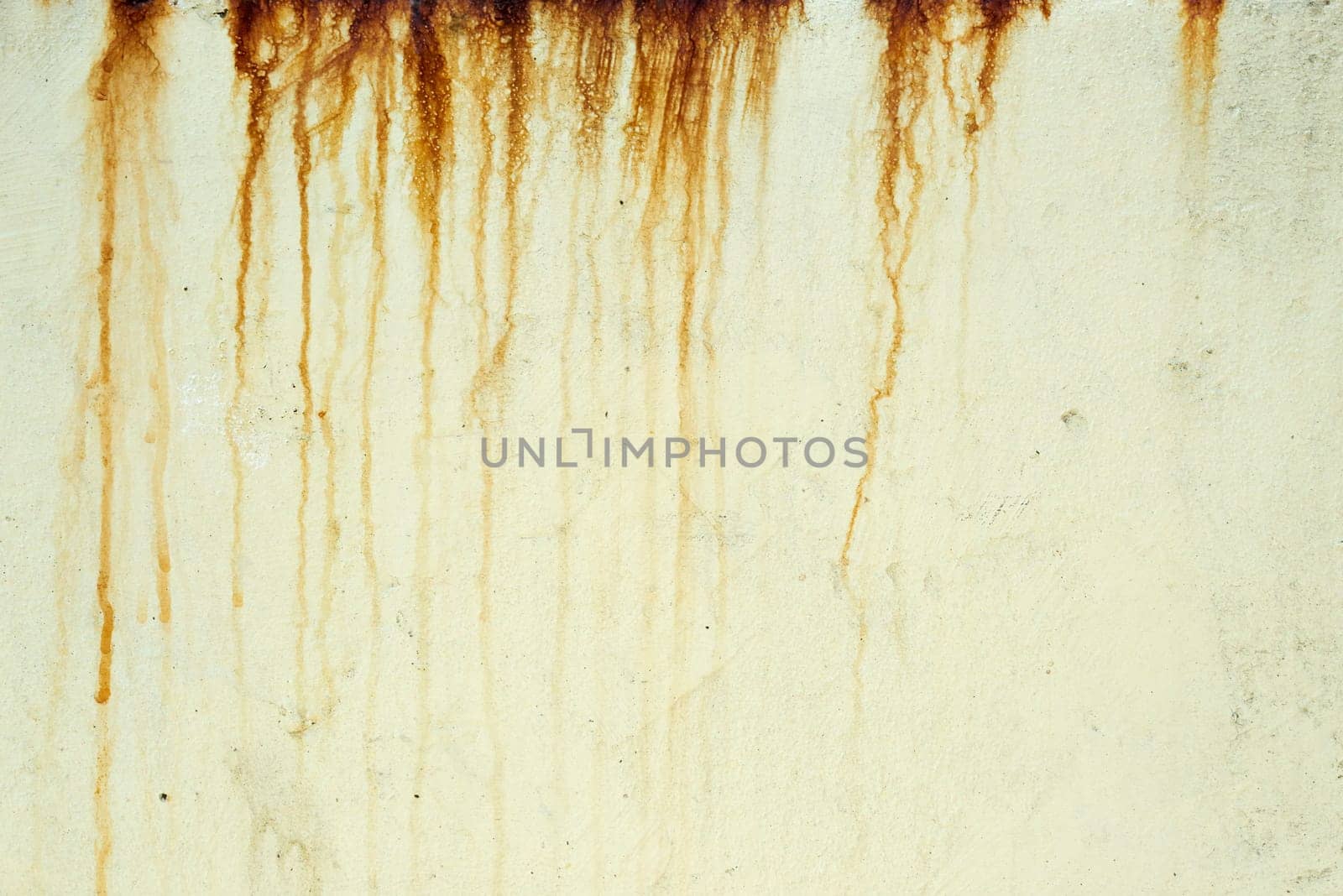 Orange and brown streaks of rust stain a light yellow textured surface