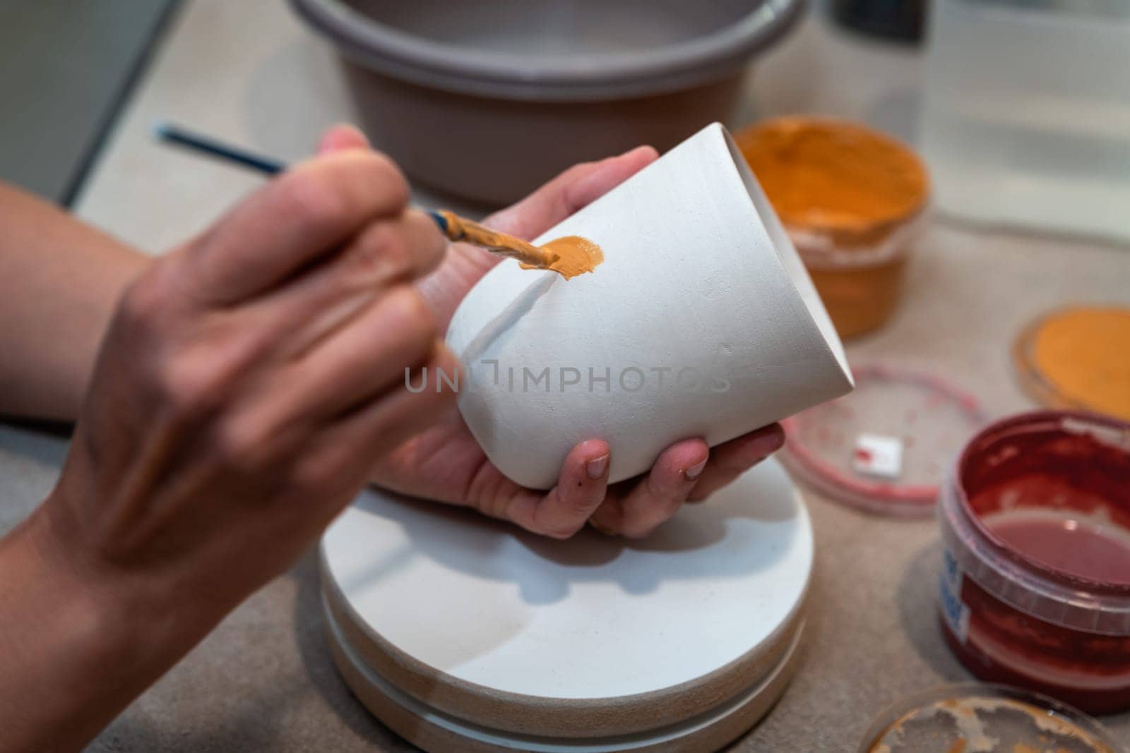 women's hands painting a pottery object