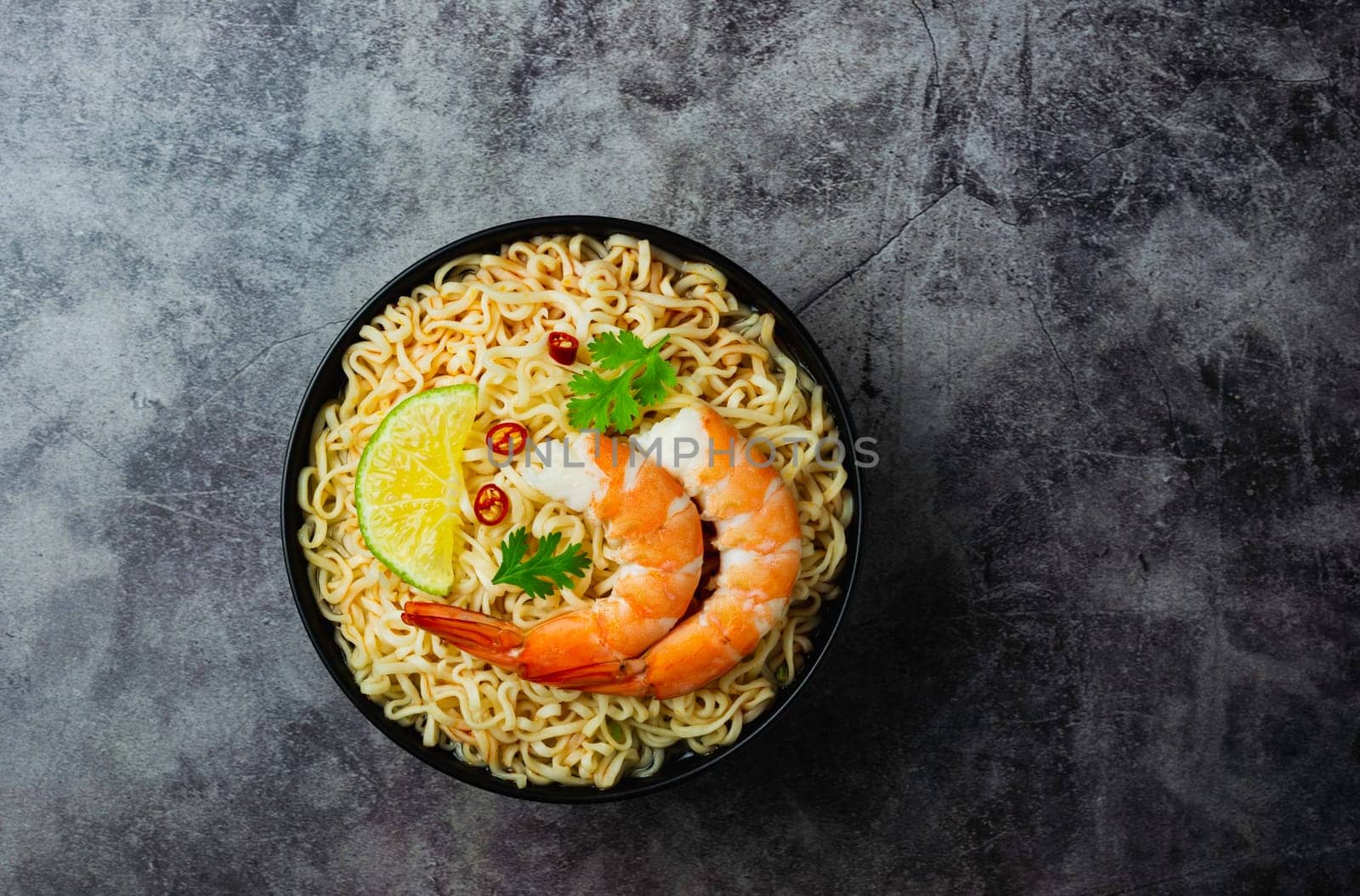 Top view of instant noodles with shrimp and chopsticks on concrete background.