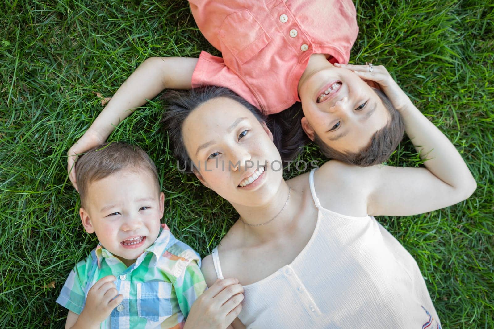 Chinese Mother and Mixed Race Children Laying On Grass.