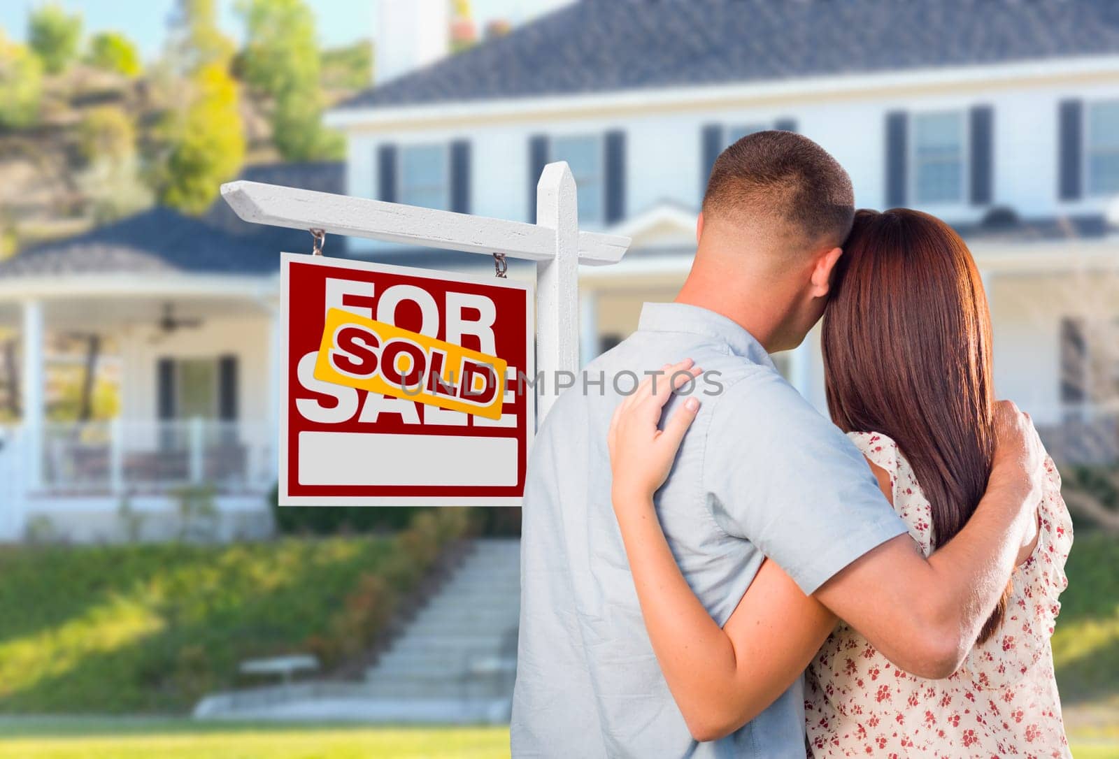 Military Couple Looking At House with Sold For Sale Real Estate Sign In Front.