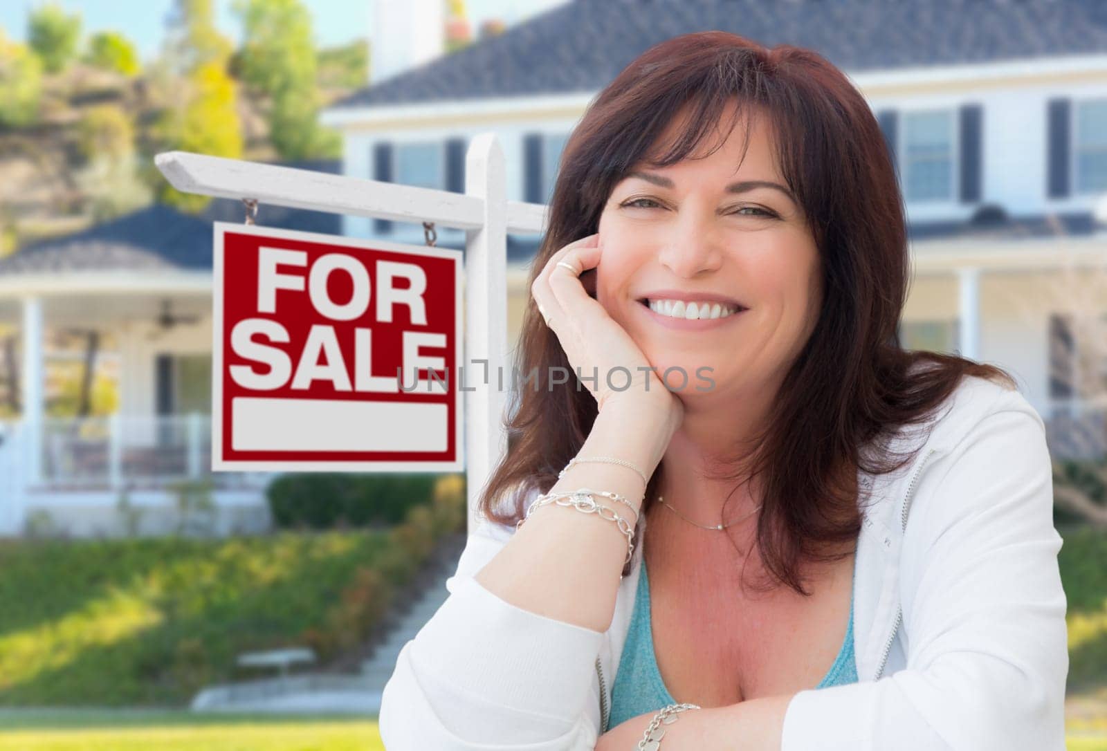 Middle Aged Woman In Front of House with For Sale Real Estate Sign In Yard.