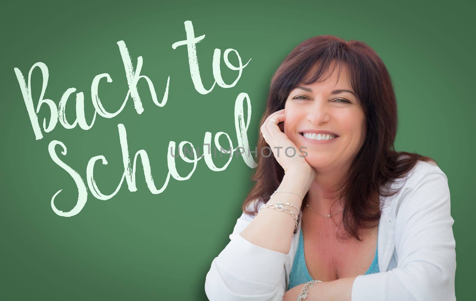 Back To School Written On Green Chalkboard Behind Smiling Middle Aged Woman.