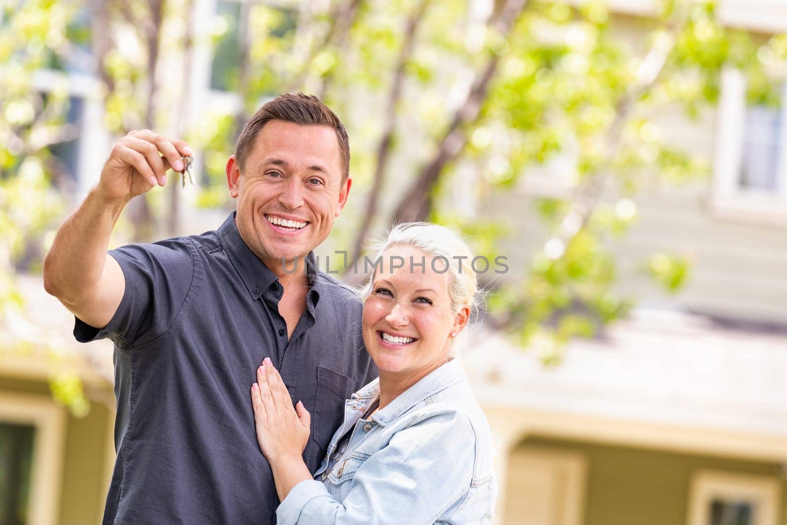 Caucasian Couple in Front of House with Keys.