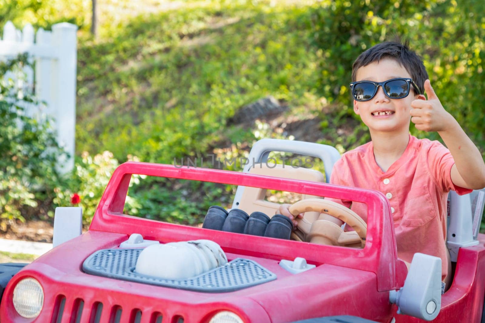 Young Mixed Race Chinese and Caucasian Boy Wearing Sunglasses Playing In Toy Car