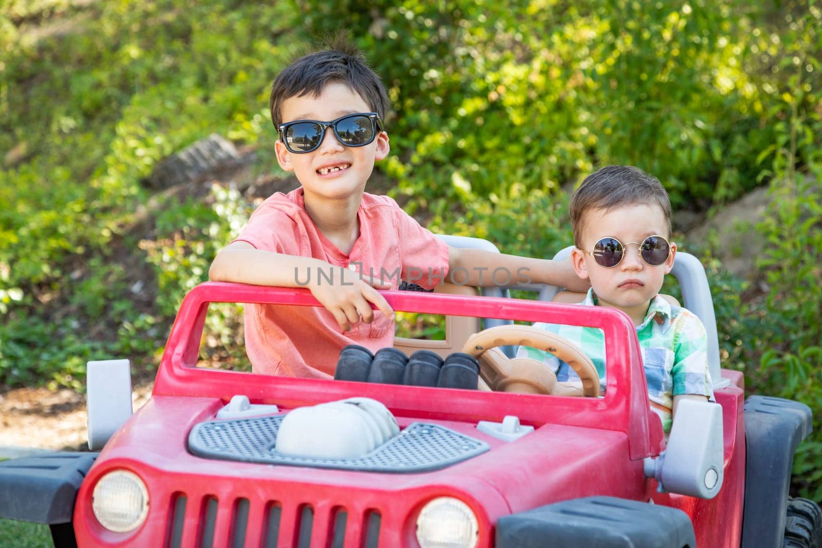Young Mixed Race Chinese and Caucasian Brothers Wearing Sunglasses Playing In Toy Car
