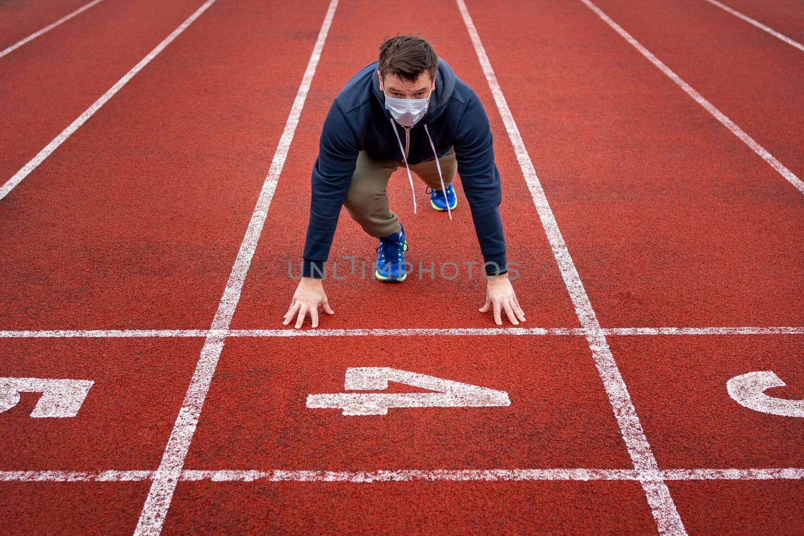 Man in surgical mask on track starting to run. Healthy fitness concept with active lifestyle.
