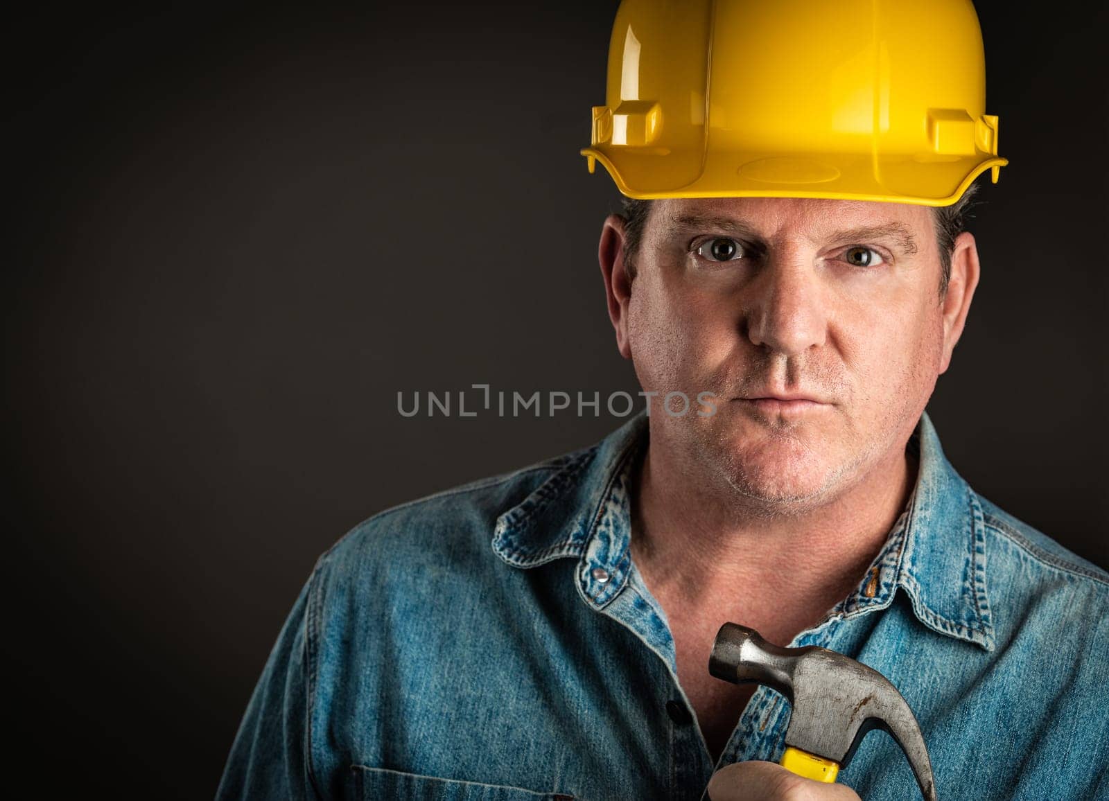 Serious Contractor in Hard Hat Holding Hammer With Dramatic Lighting.