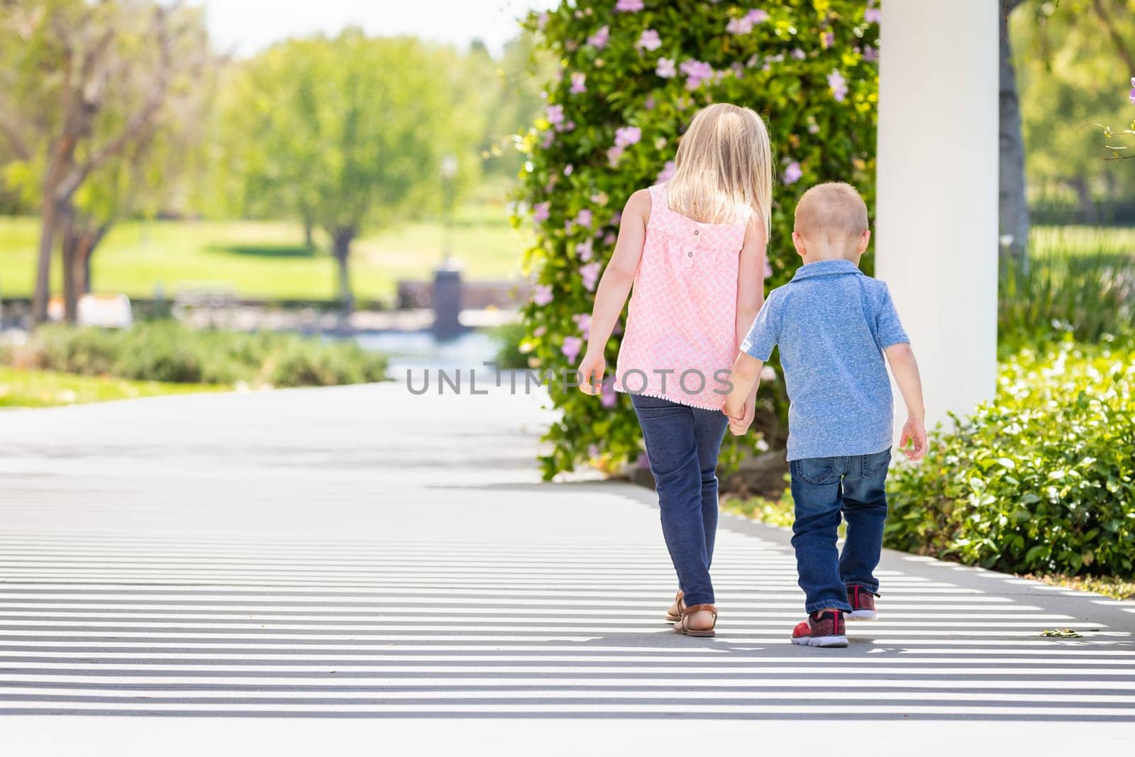 Young Sister and Brother Holding Hands And Walking At The Park.
