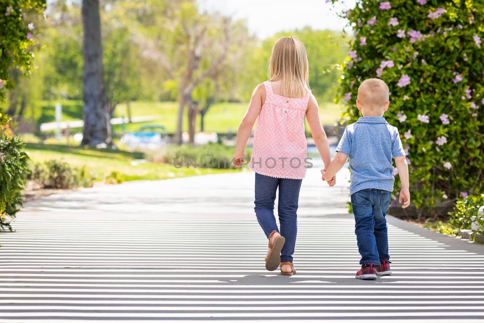 Young Sister and Brother Holding Hands And Walking At The Park.