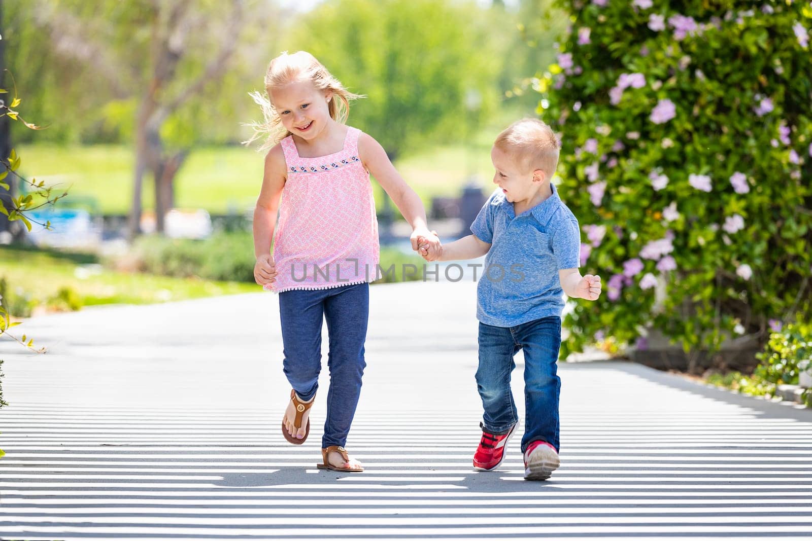 Young Sister and Brother Holding Hands And Running At The Park.