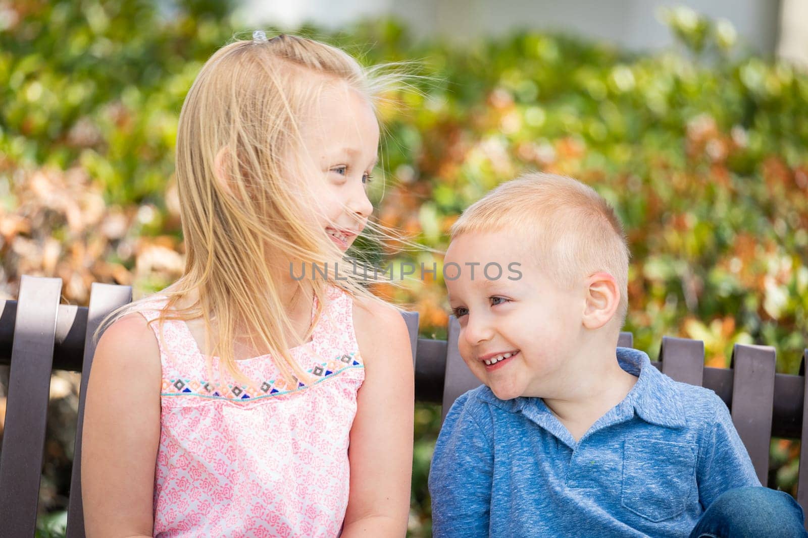 Young Sister and Brother Having Fun On The Bench At The Park.