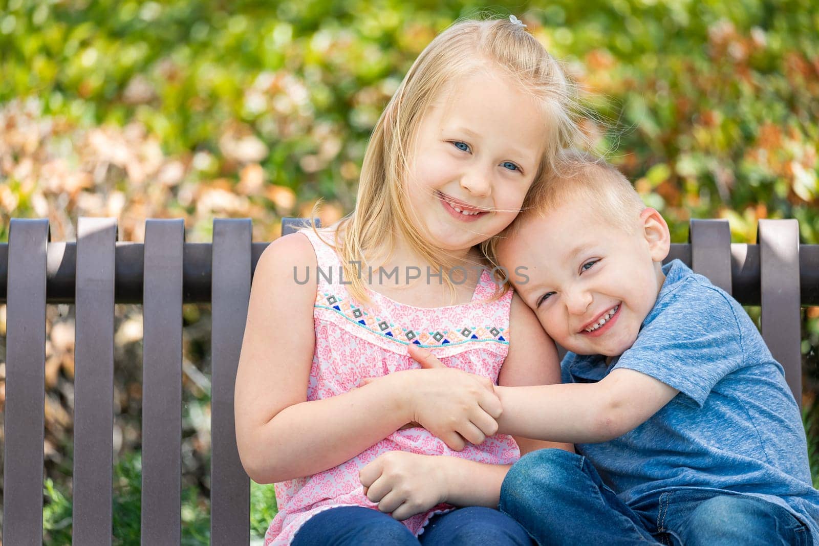 Young Sister and Brother Having Fun On The Bench At The Park.