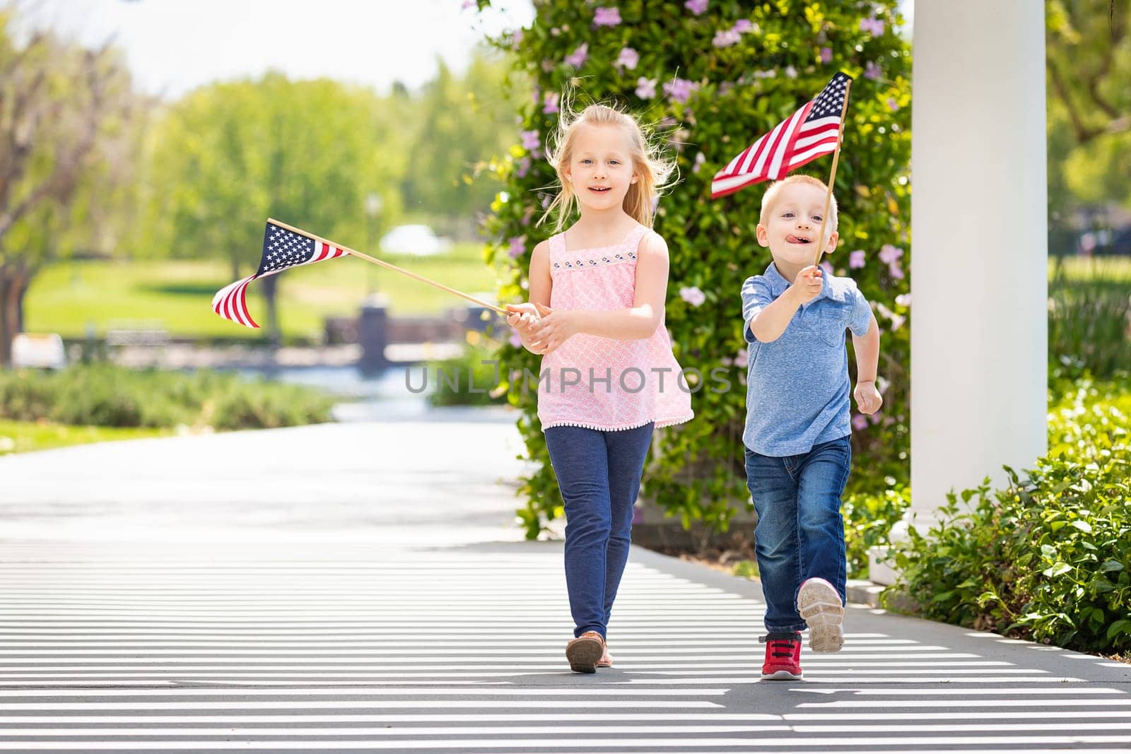Young Sister and Brother Waving American Flags At The Park.