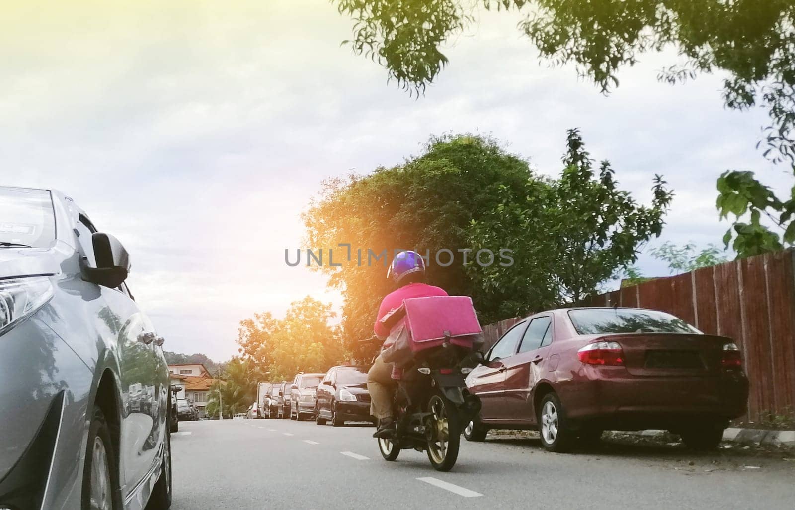 Motorbike delivery man with isothermal food pink case box  delivering food in an asian city.Express food delivery service.