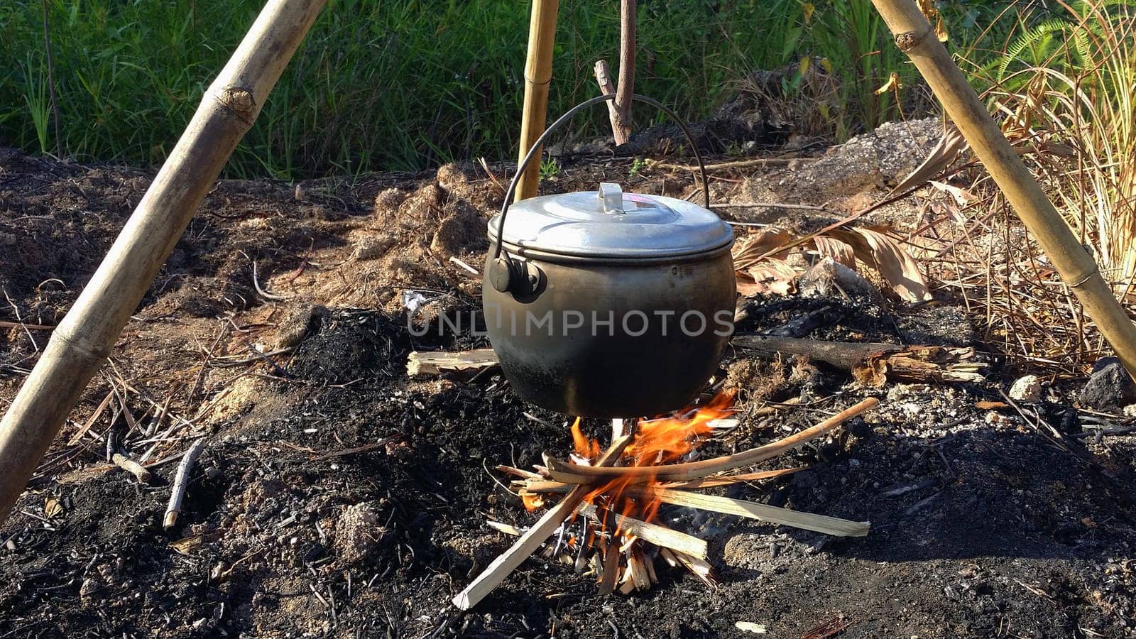 Preparing and cooking food in field conditions, boiling pot at the campfire on picnic in the forest during summer holiday.