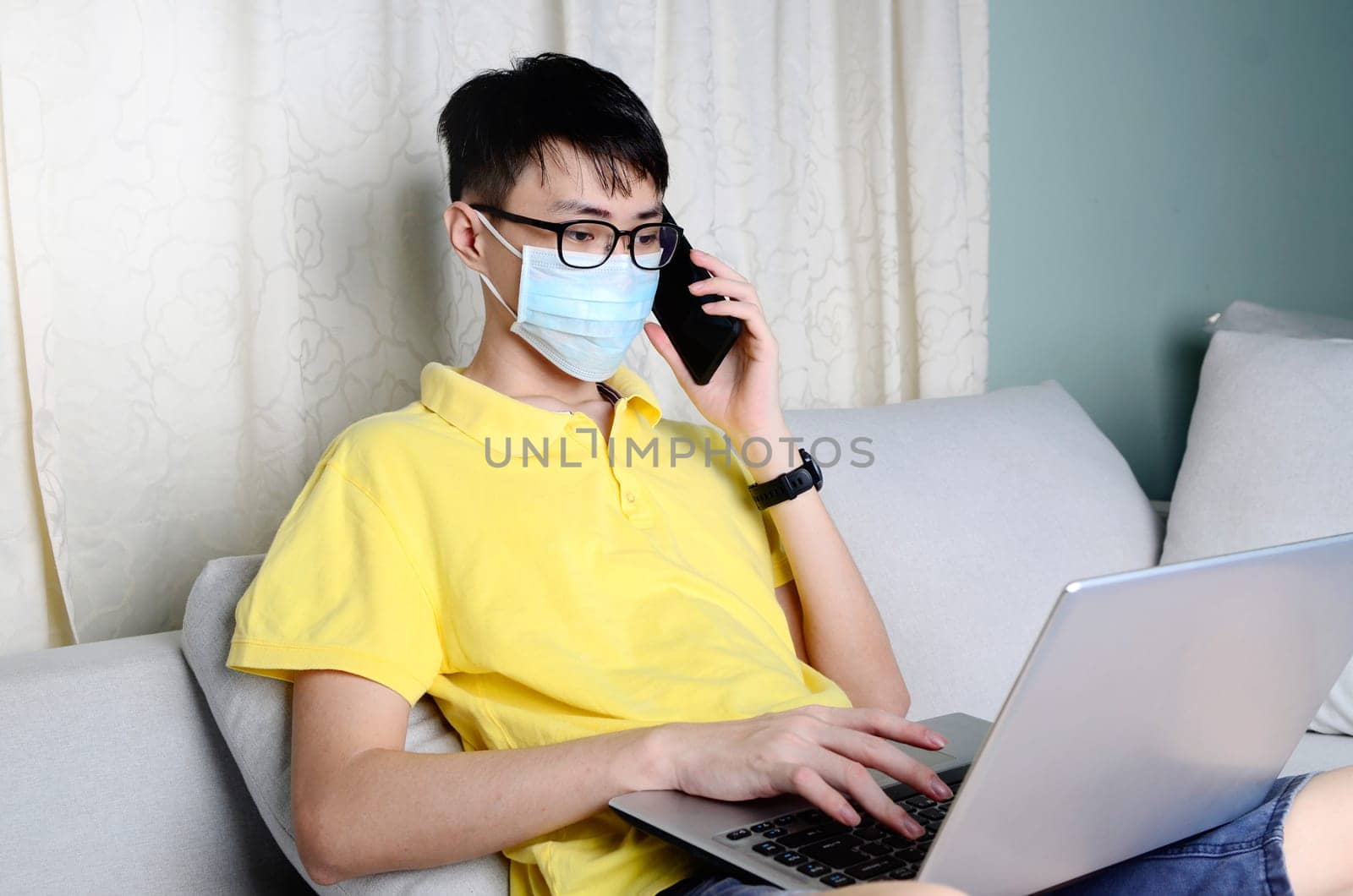 An asian man is working from home during pandemic coronavirus  Covid-19. Ccoronavirus covid 19 infected patient in quarantine room using smartphone and  computer.....