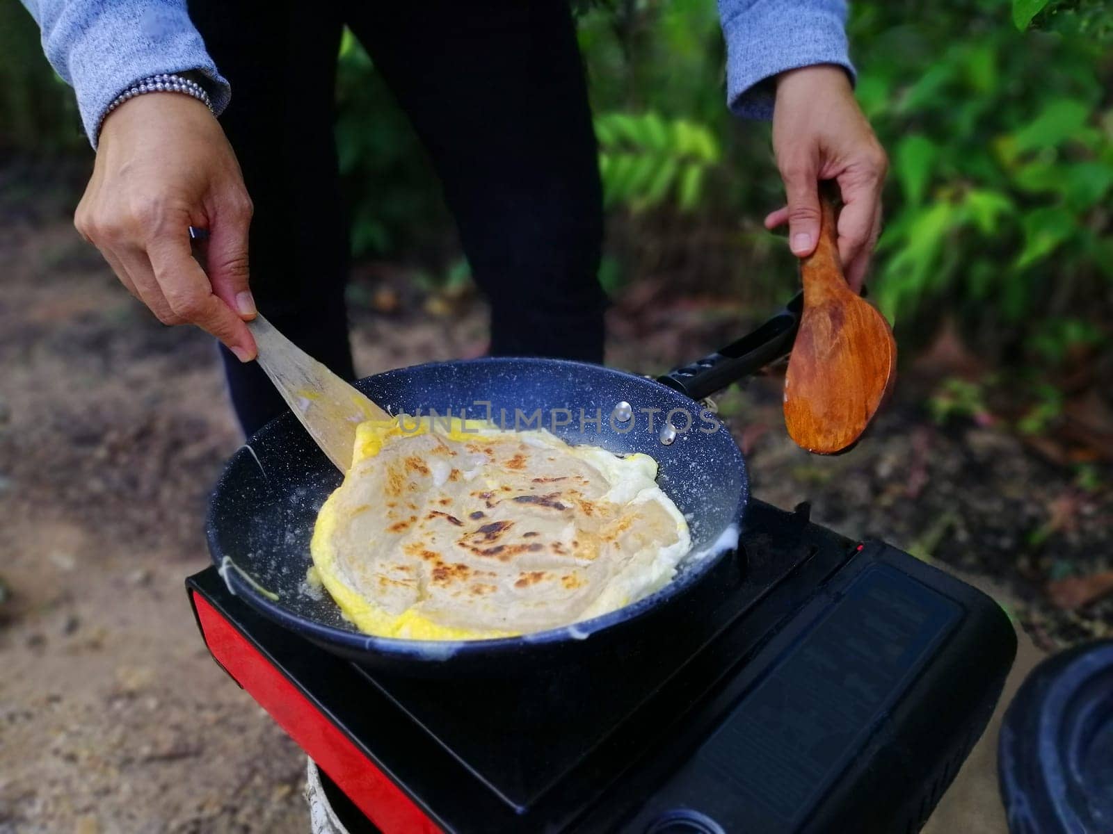 Asian woman cooking roti canai at forest during outdoor camping.