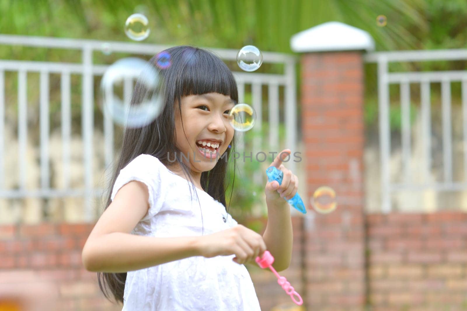 Lovely little asian girl blowing soap bubbles, Outdoor portrait.