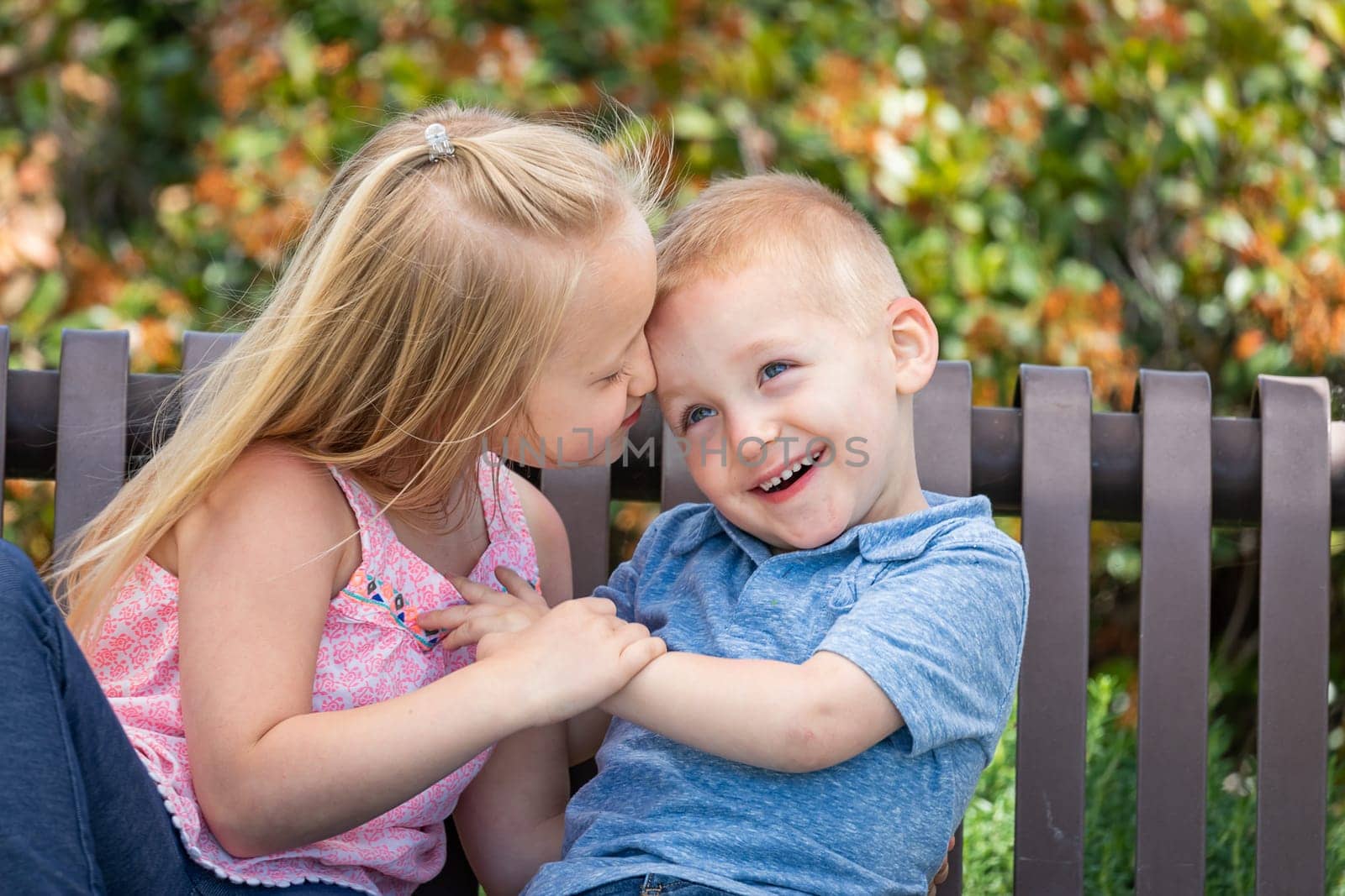 Young Sister and Brother Having Fun On The Bench At The Park.