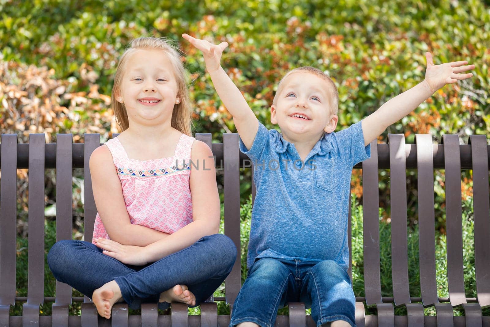 Young Sister and Brother Having Fun On The Bench At The Park.
