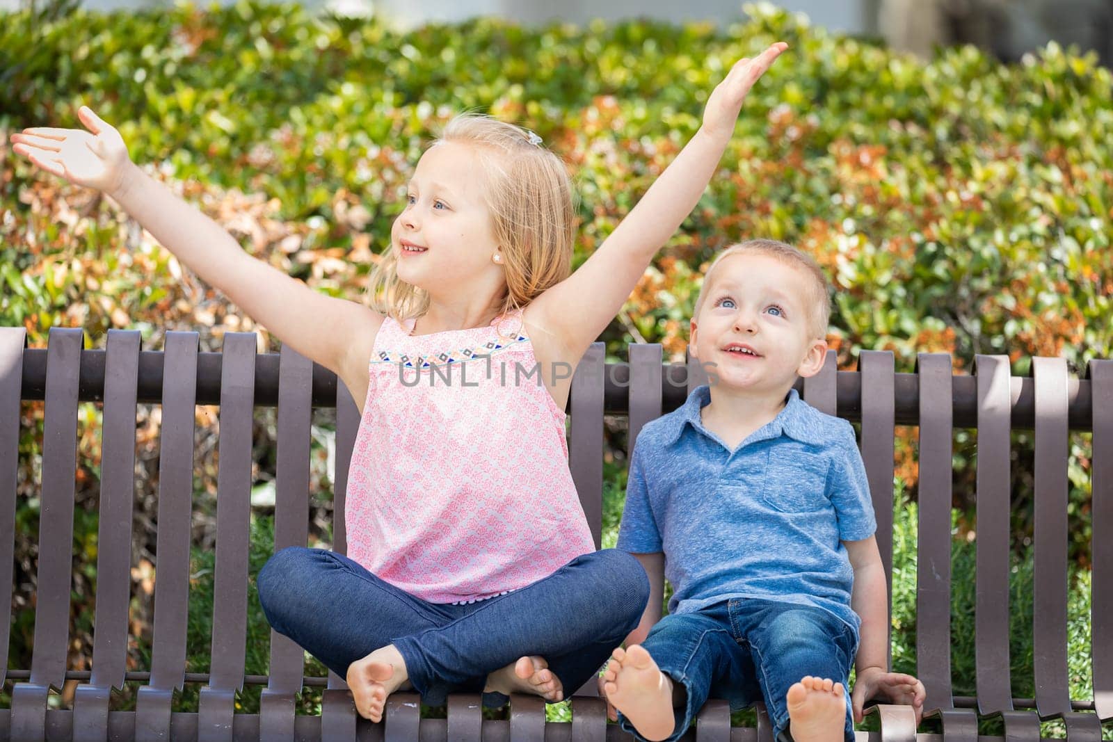 Young Sister and Brother Having Fun On The Bench At The Park.
