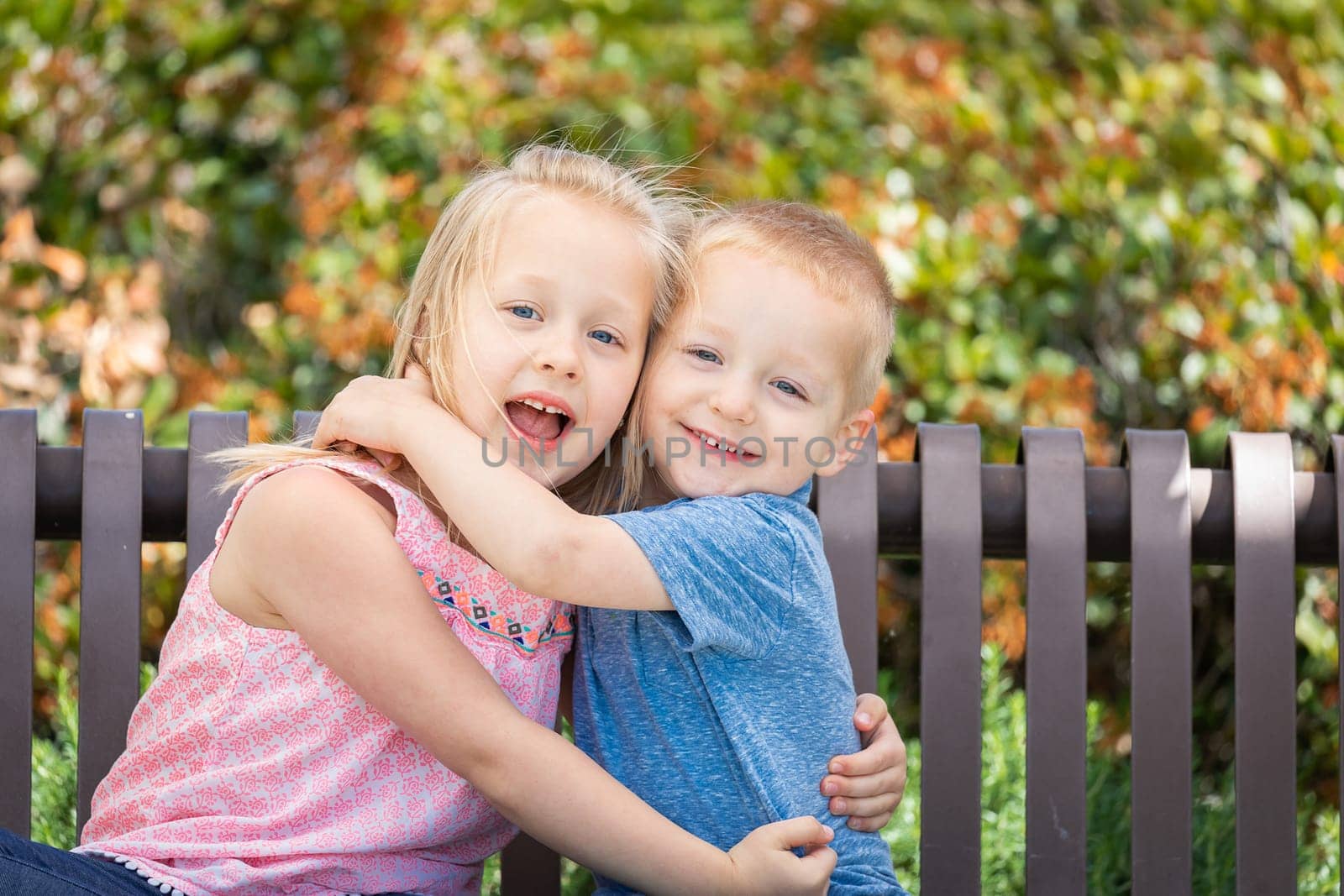 Young Sister and Brother Having Fun On The Bench At The Park.