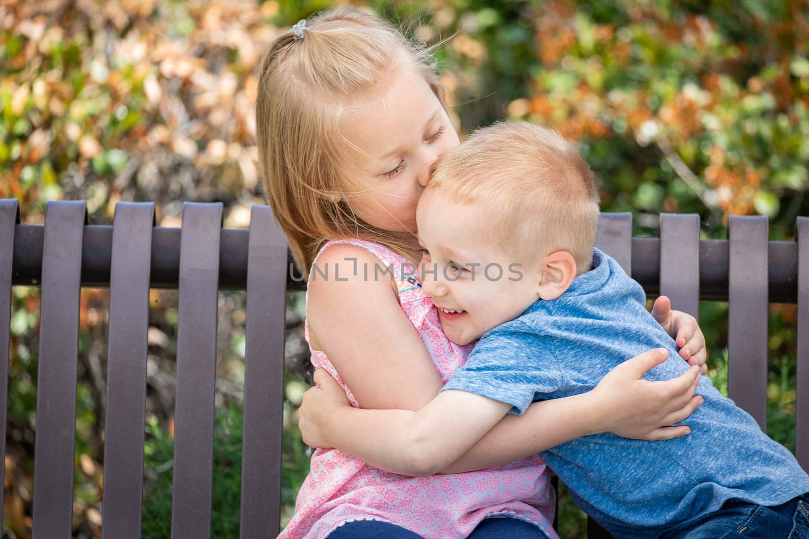Young Sister and Brother Having Fun On The Bench At The Park.