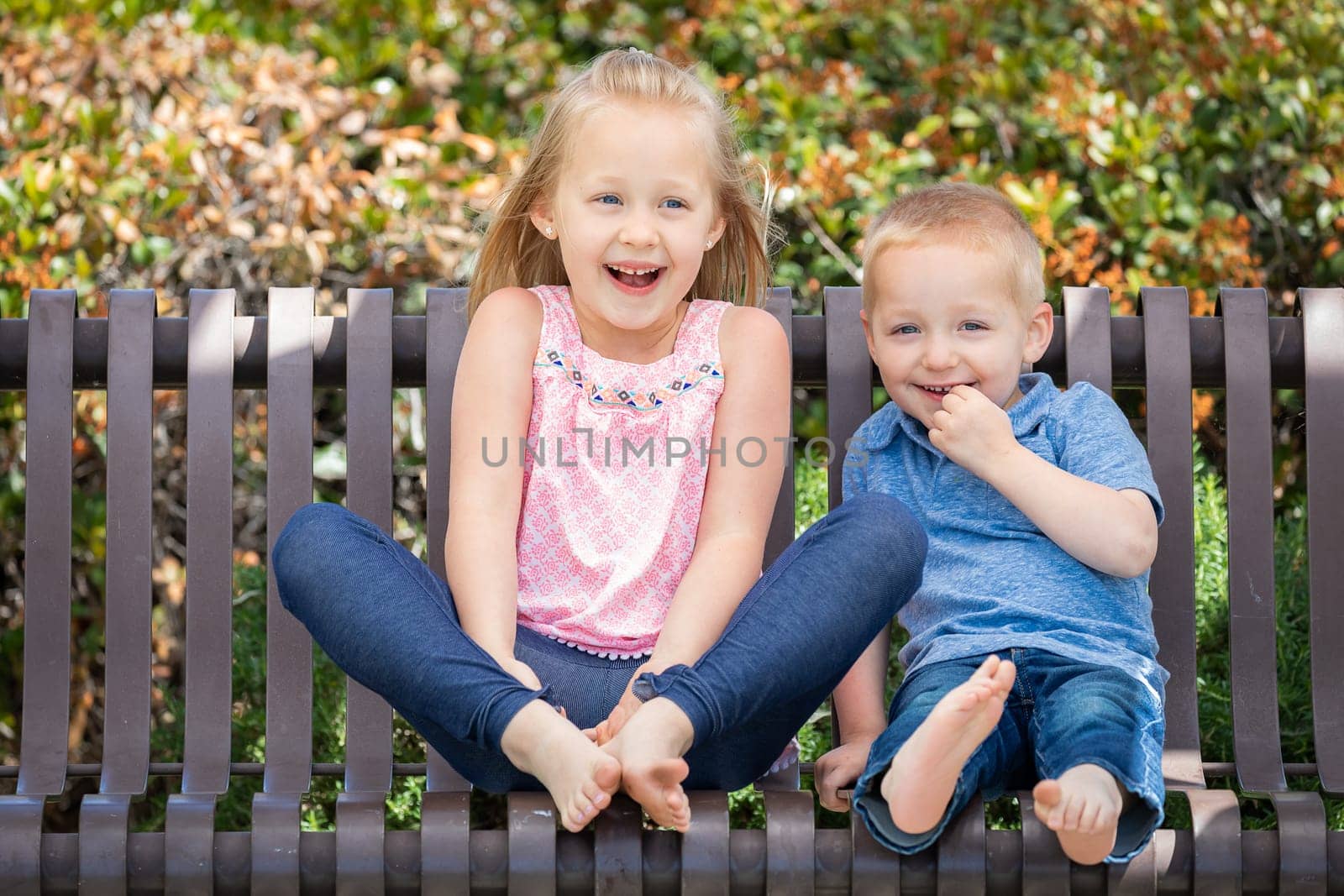 Young Sister and Brother Having Fun On The Bench At The Park.