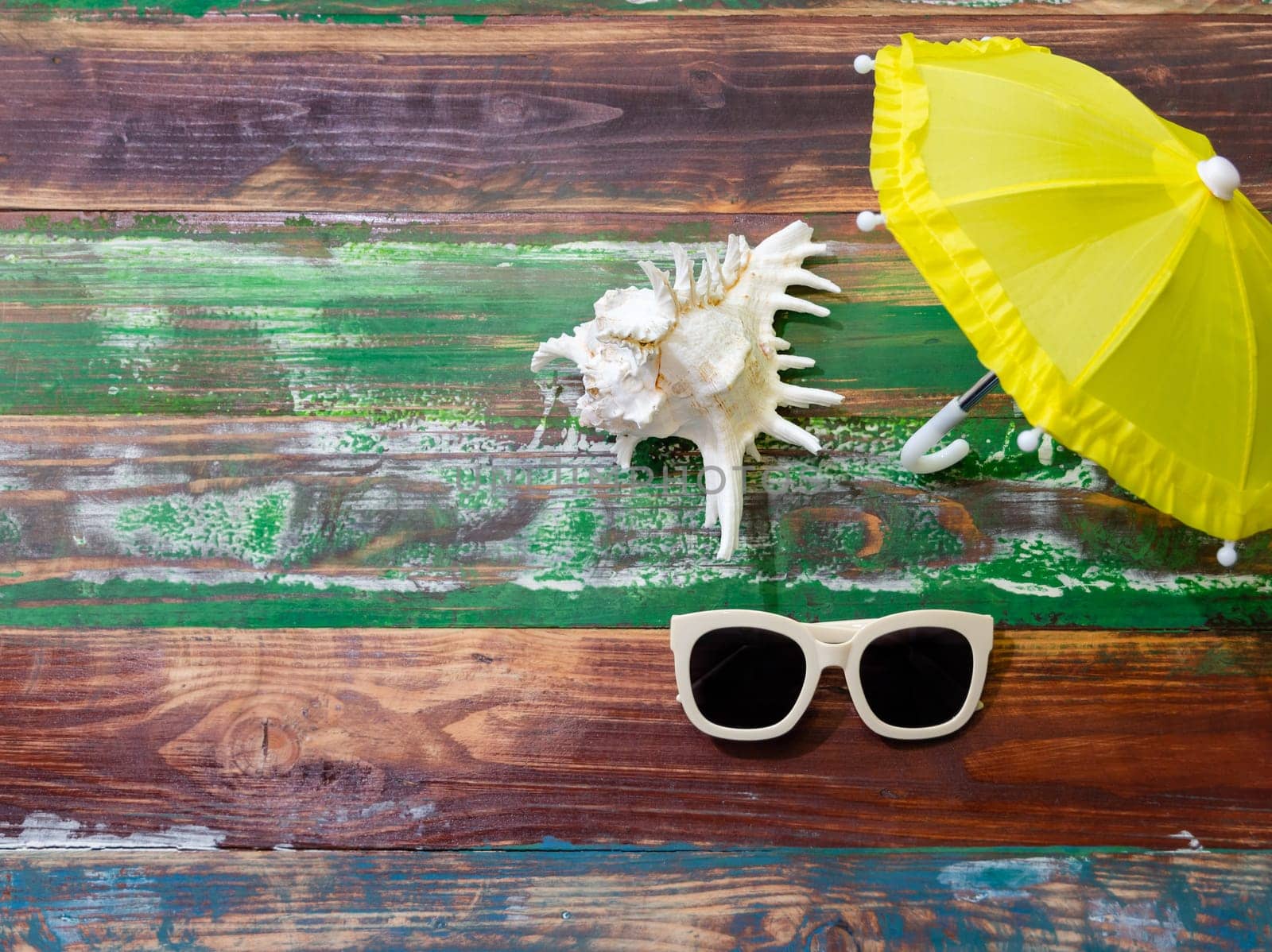 Summer background with beach accessories of white sunglasses and yellow umbrella on weathered wooden background