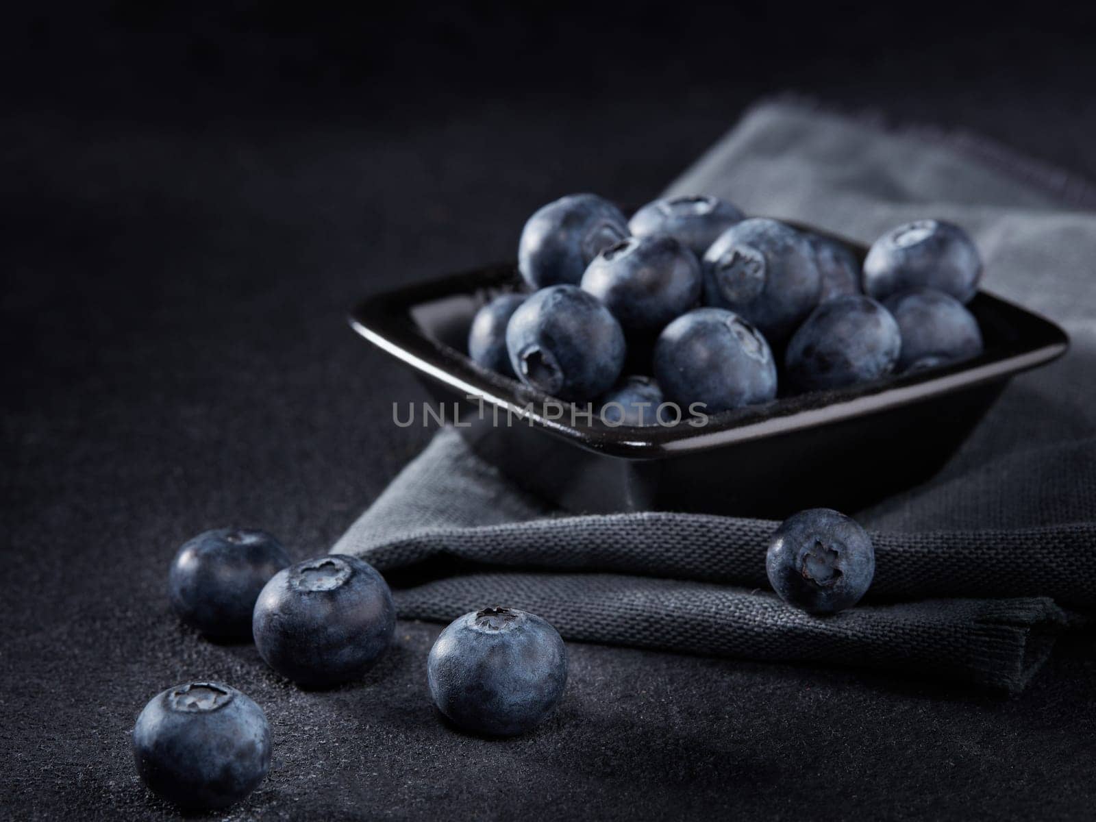 Ripe blueberries (bog whortleberry, great bilberry) in black bowl on dark grey background. Selective focus on blueberies lying on table