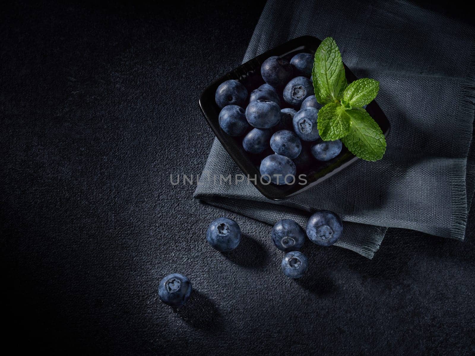 Ripe blueberries (bog whortleberry, great bilberry) with mint in black bowl on dark grey background. Top view