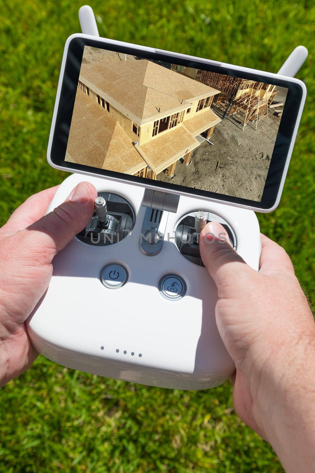 Hands Holding Drone Quadcopter Controller With Construction House Framing on Screen.