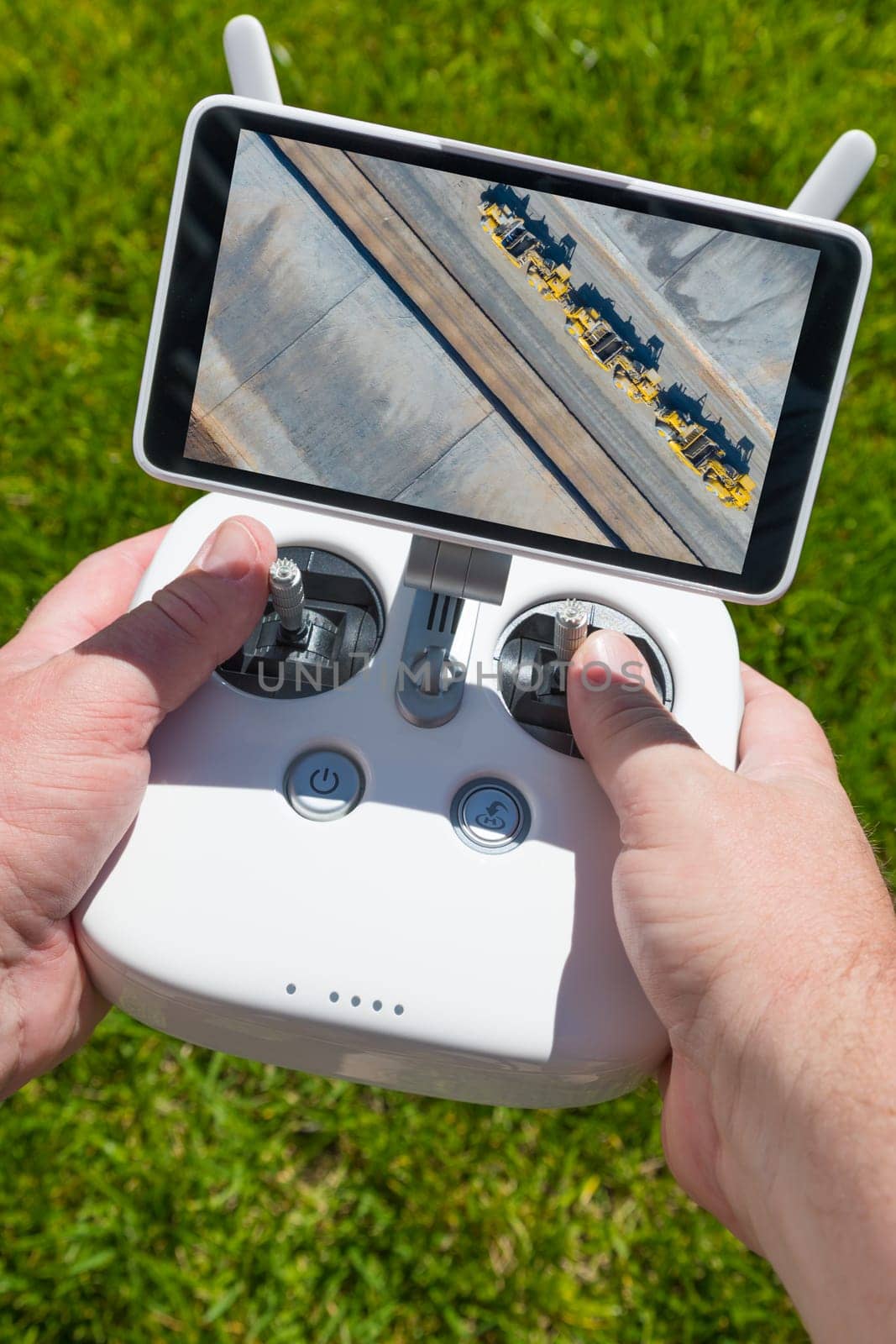 Hands Holding Drone Quadcopter Controller With Overhead of Tractors on Screen.