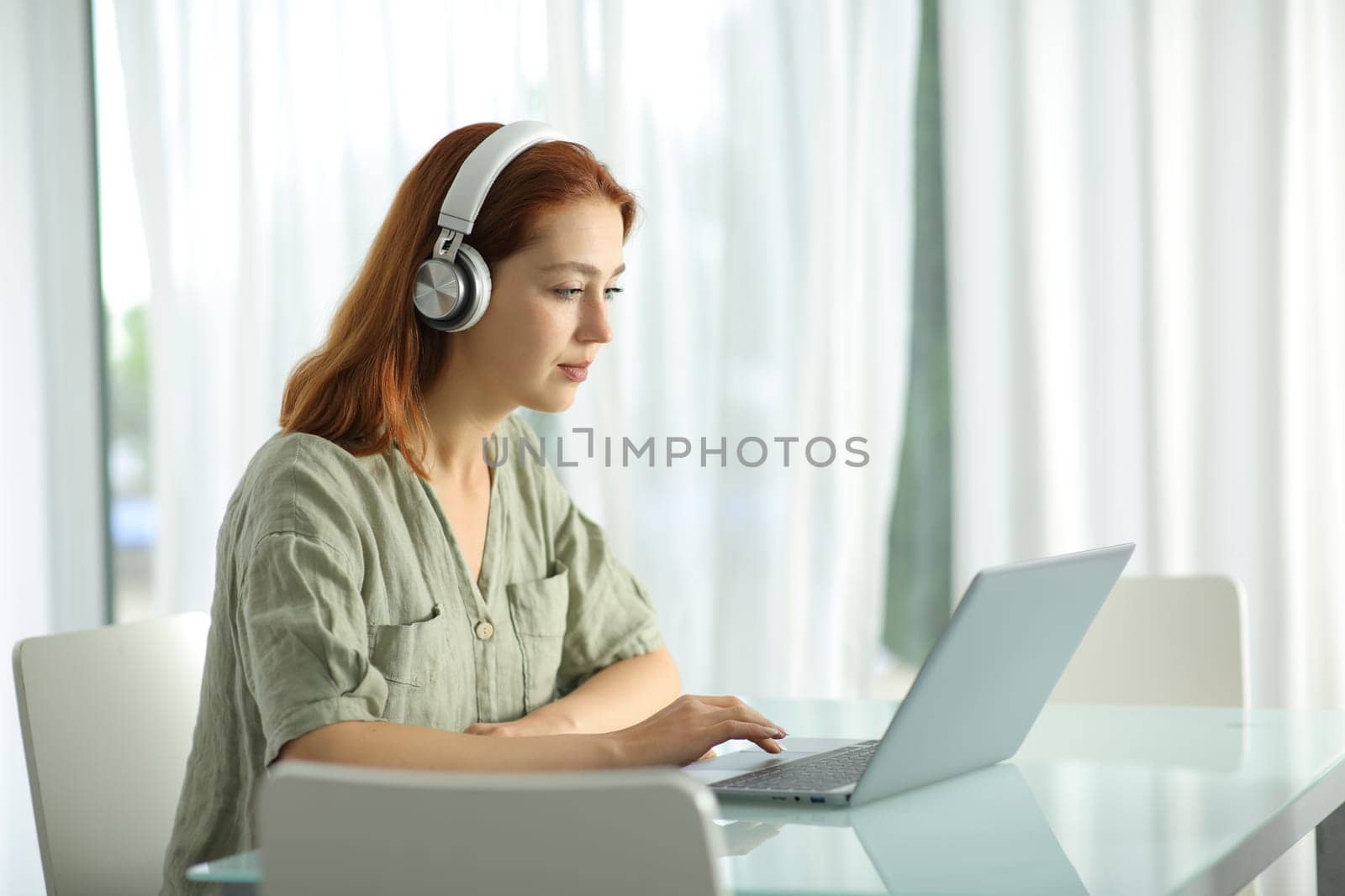 Woman with headphones checking laptop at home